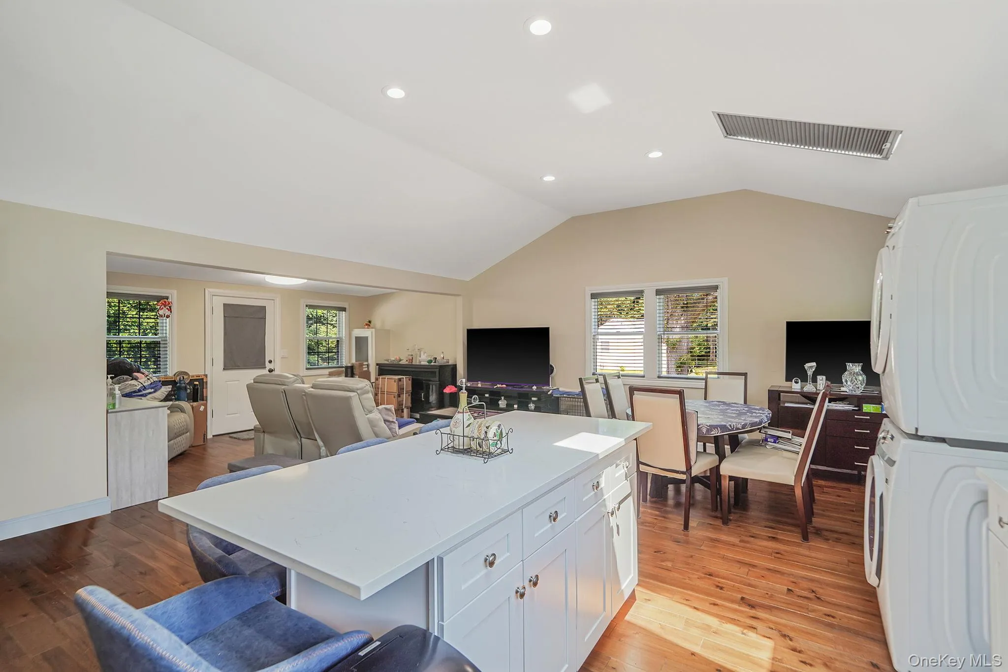 Kitchen featuring stacked washing machine and dryer, vaulted ceiling, white cabinets, a center island, and light countertops Kitchen featuring stacked washing machine and dryer, vaulted ceiling, white cabinets, a center island, and light countertops