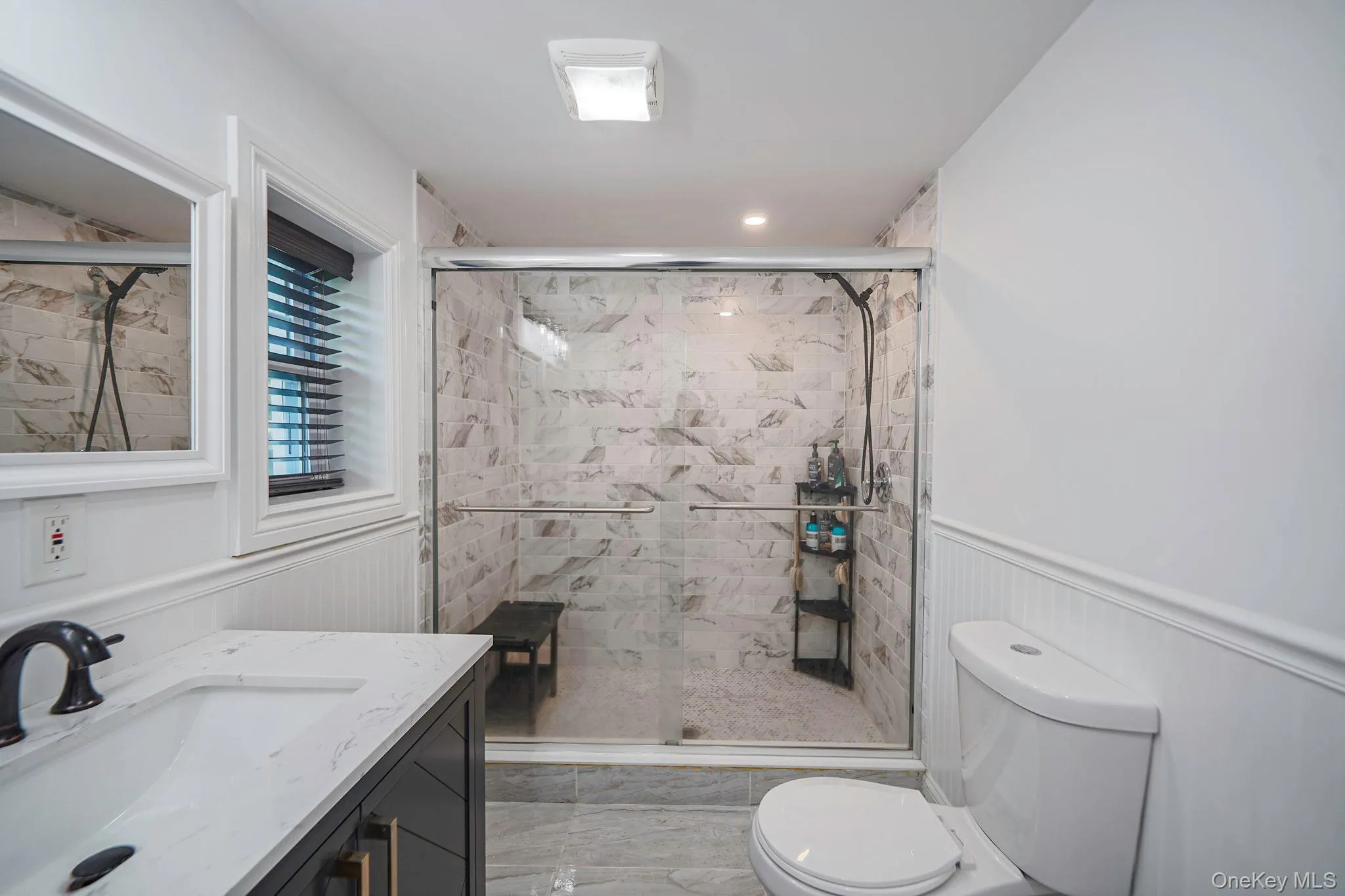 Full bathroom featuring vanity, marble finish flooring, a stall shower, and a wainscoted wall Full bathroom featuring vanity, marble finish flooring, a stall shower, and a wainscoted wall