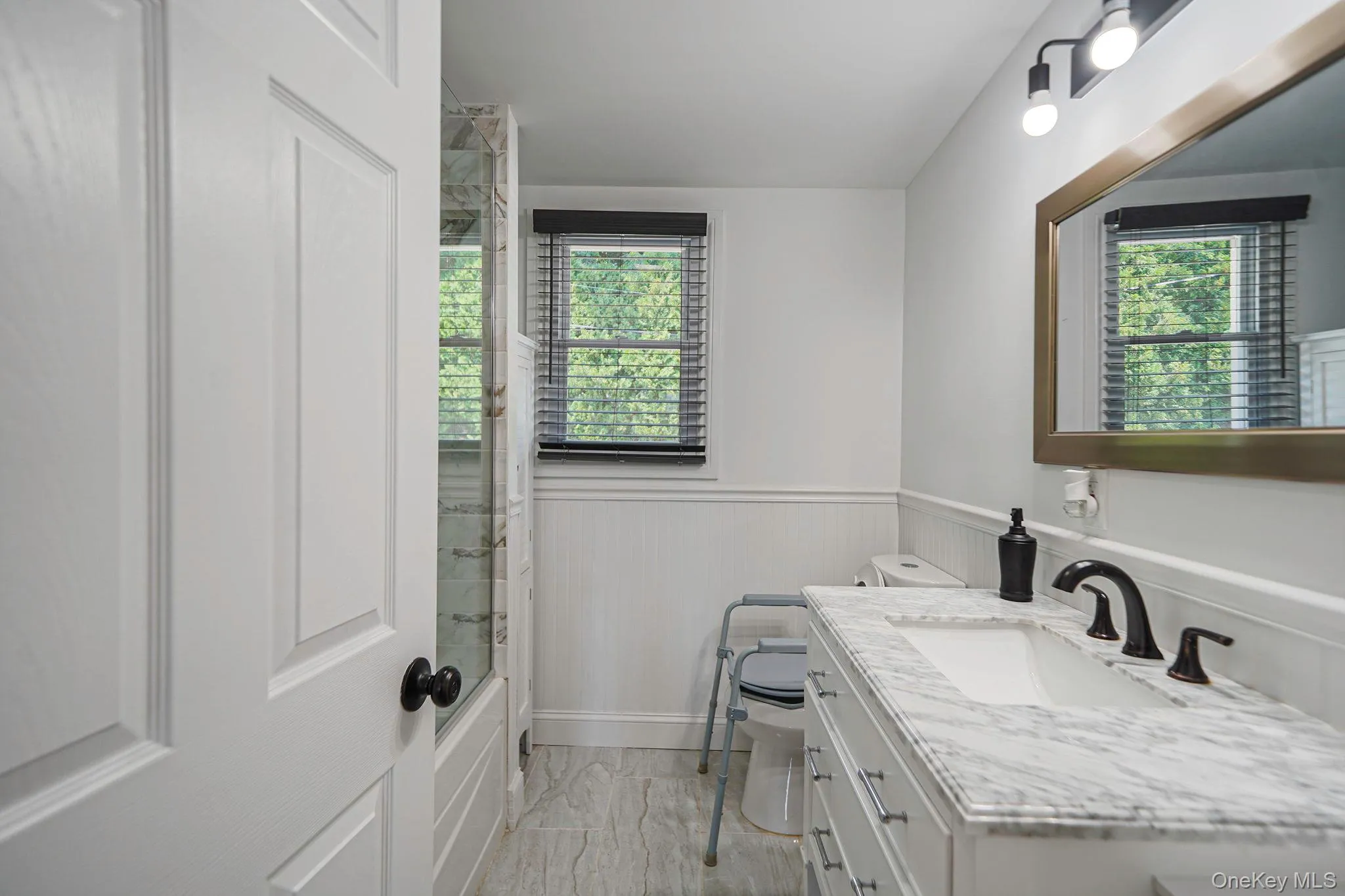 Bathroom featuring marble finish flooring, vanity, wainscoting, healthy amount of natural light, and shower / bathtub combination Bathroom featuring marble finish flooring, vanity, wainscoting, healthy amount of natural light, and shower / bathtub combination