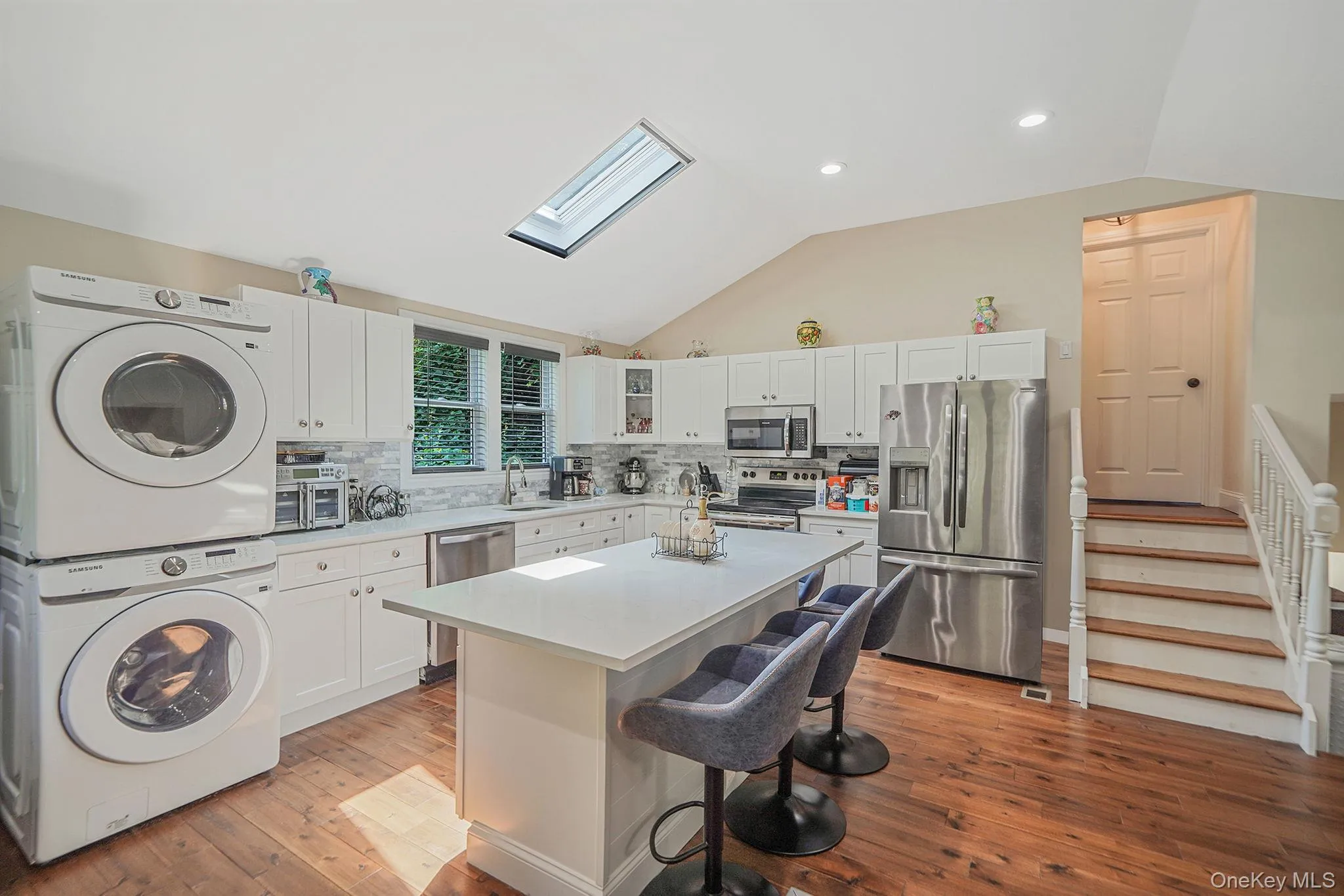 Kitchen with stacked washer / dryer, appliances with stainless steel finishes, vaulted ceiling, a breakfast bar, and a skylight Kitchen with stacked washer / dryer, appliances with stainless steel finishes, vaulted ceiling, a breakfast bar, and a skylight