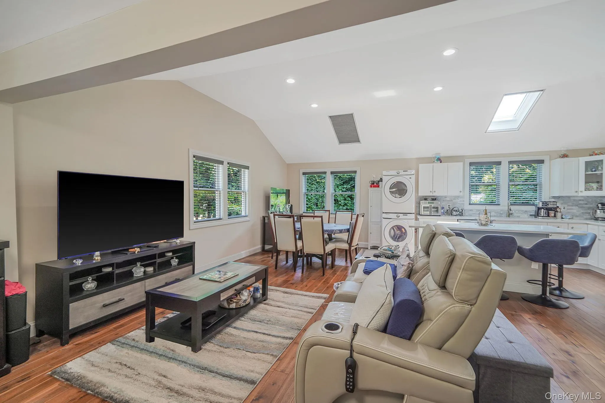Living area with stacked washer / dryer, lofted ceiling, light wood-style flooring, and recessed lighting Living area with stacked washer / dryer, lofted ceiling, light wood-style flooring, and recessed lighting