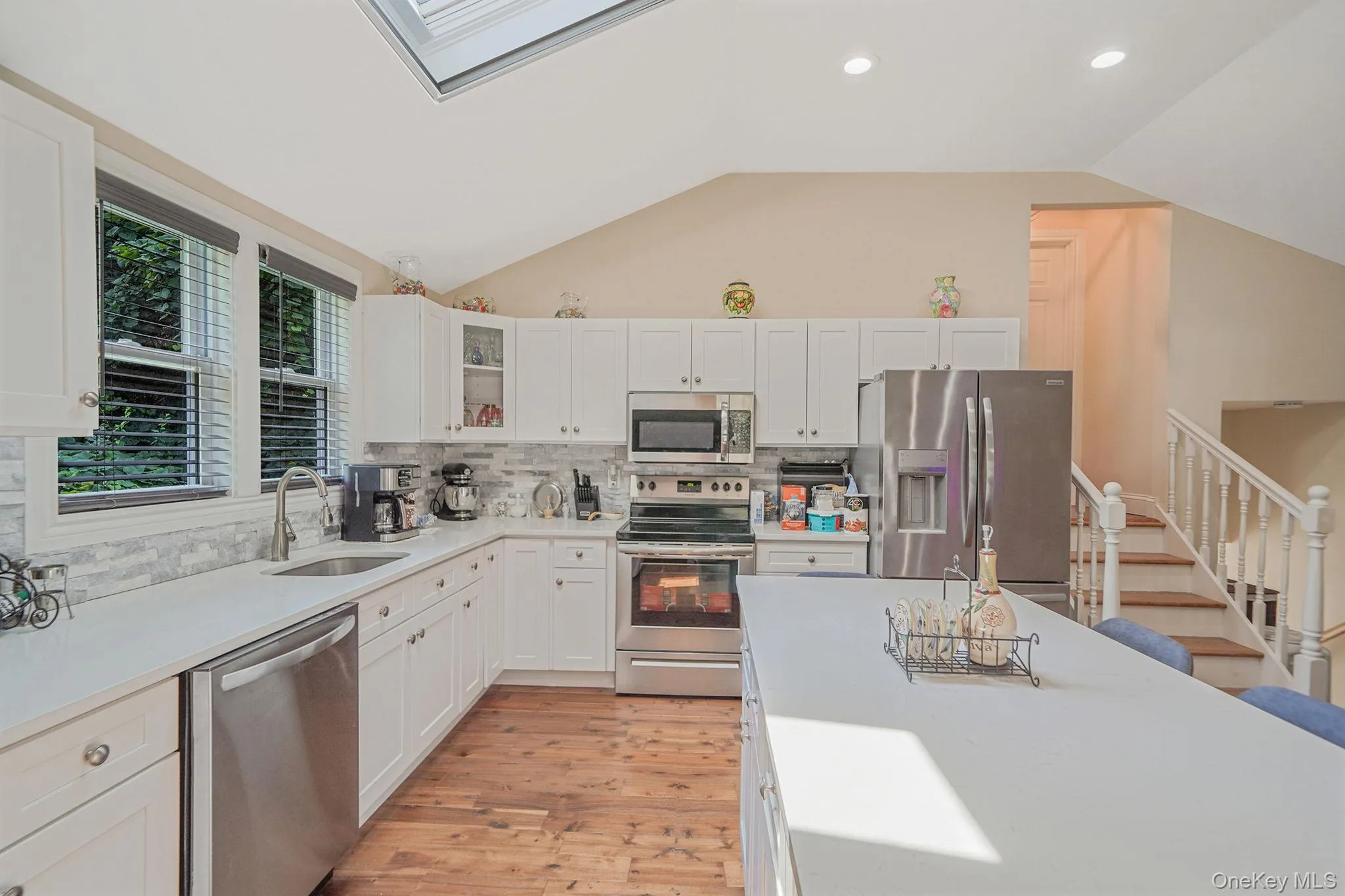 Kitchen with appliances with stainless steel finishes, vaulted ceiling, light wood-style floors, white cabinetry, and tasteful backsplash Kitchen with appliances with stainless steel finishes, vaulted ceiling, light wood-style floors, white cabinetry, and tasteful backsplash