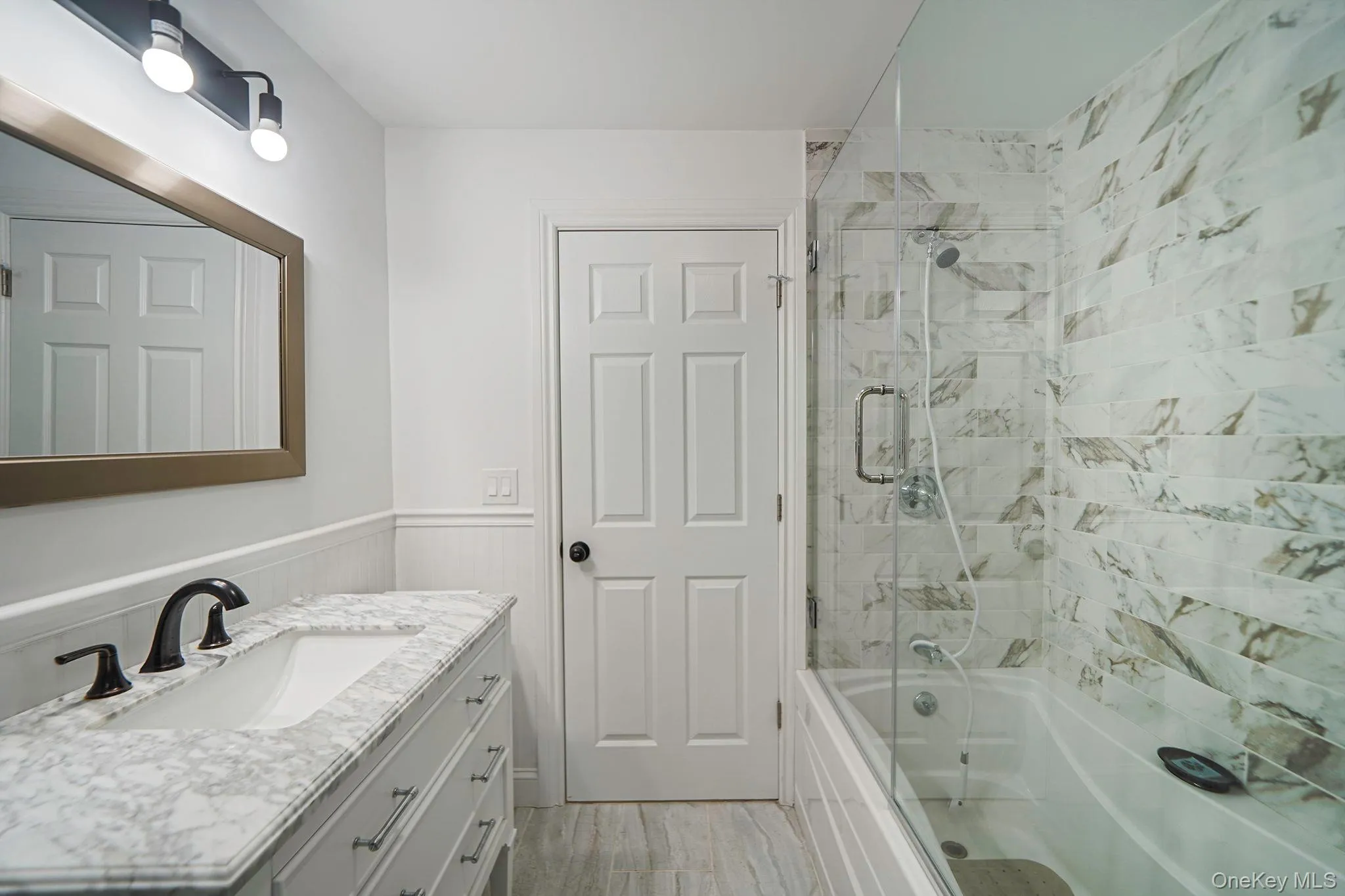 Bathroom with vanity, shower / bath combination with glass door, and a wainscoted wall Bathroom with vanity, shower / bath combination with glass door, and a wainscoted wall