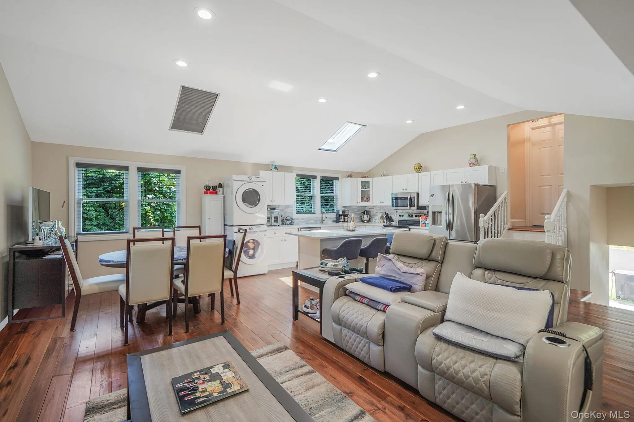 Living room with stacked washer / dryer, lofted ceiling, light wood-type flooring, and recessed lighting Living room with stacked washer / dryer, lofted ceiling, light wood-type flooring, and recessed lighting