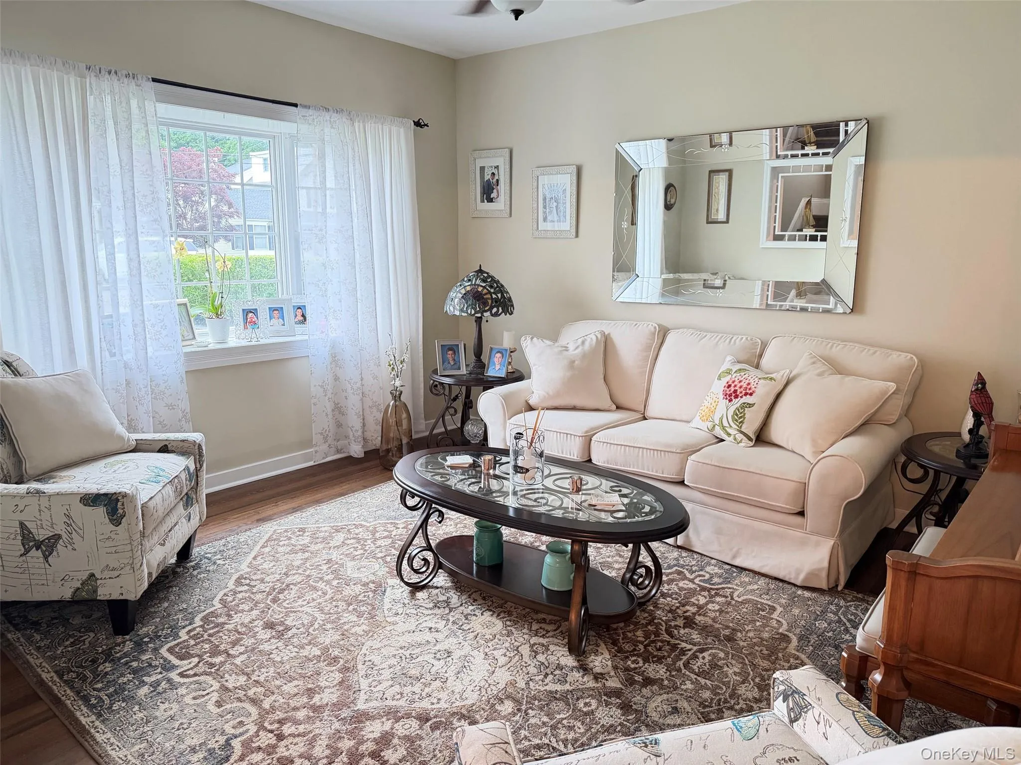 Living area featuring wood-finish flooring, a large window with white trim, and a decorative area rug Living area featuring wood-finish flooring, a large window with white trim, and a decorative area rug