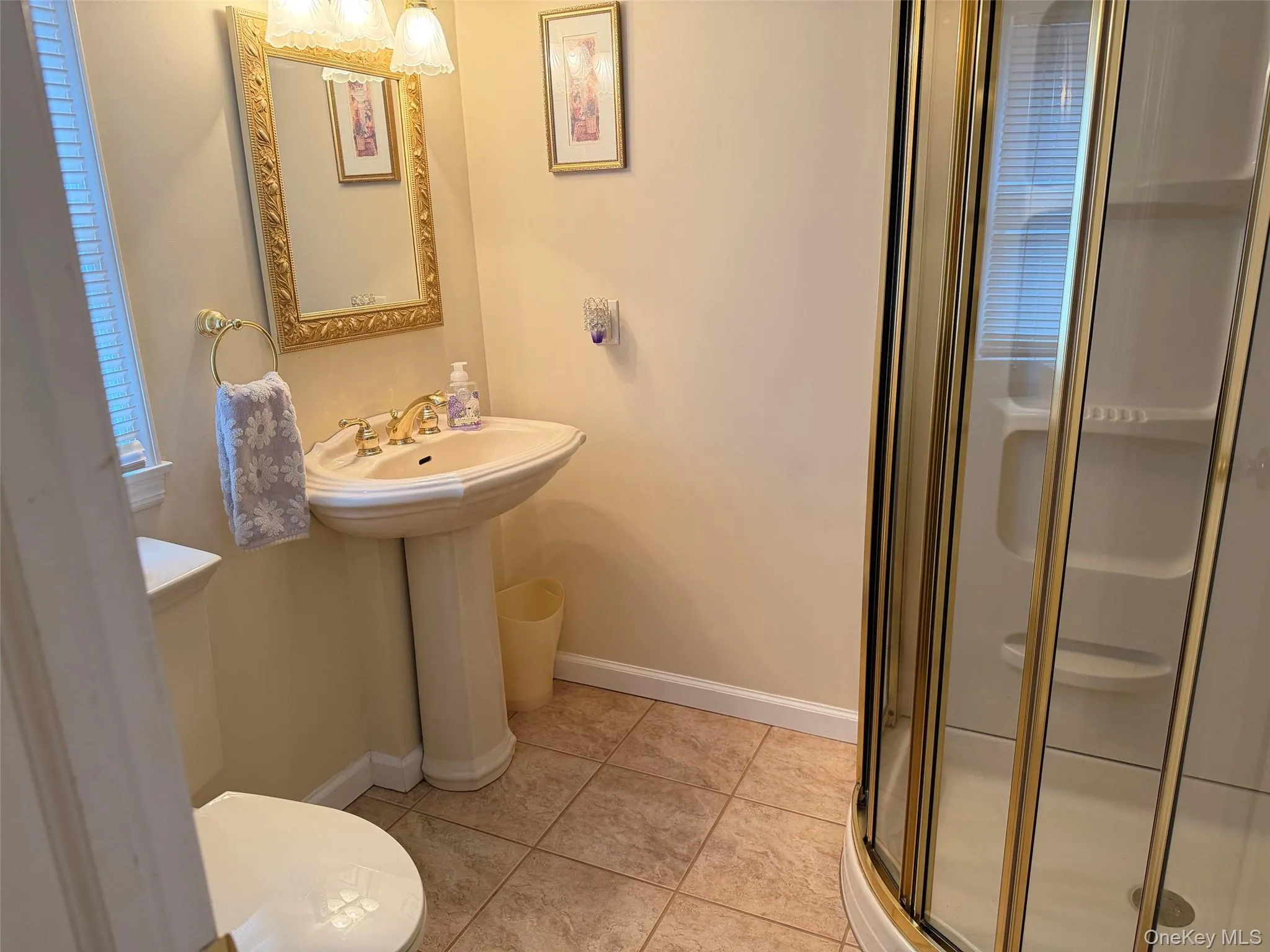 Bathroom featuring a pedestal sink with brass-finish faucet, a framed mirror, and an enclosed shower with brass-finish hardware Bathroom featuring a pedestal sink with brass-finish faucet, a framed mirror, and an enclosed shower with brass-finish hardware