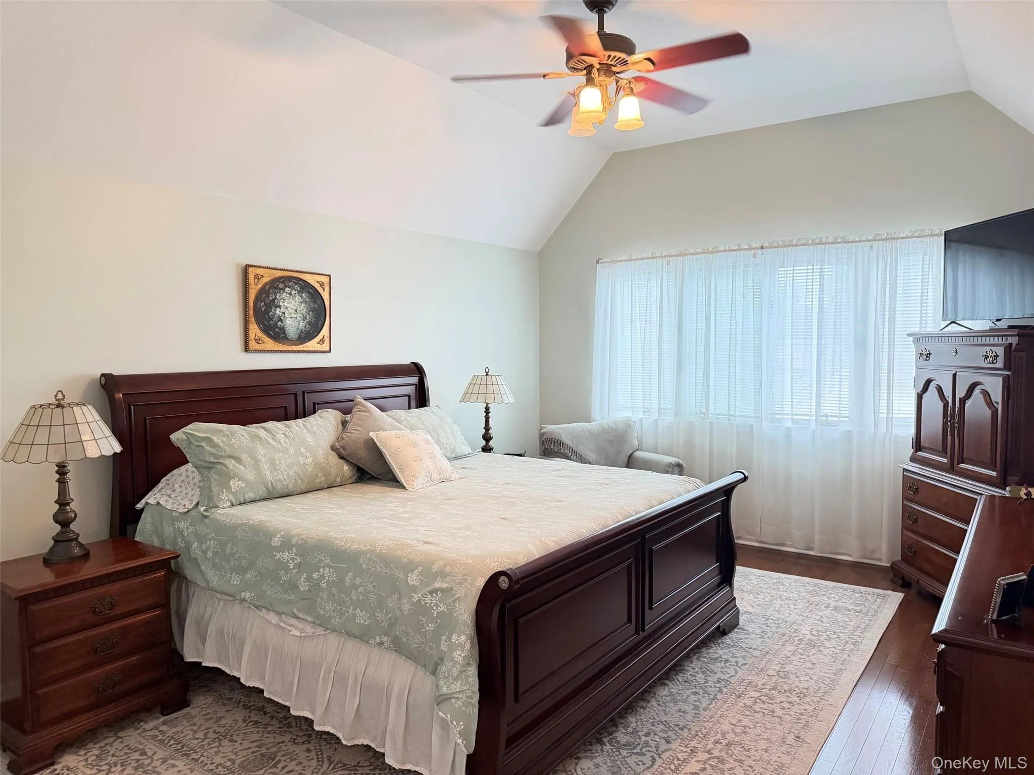 Vaulted ceiling with a ceiling fan light fixture, wood-finish flooring, and a large window with sheer privacy curtains Vaulted ceiling with a ceiling fan light fixture, wood-finish flooring, and a large window with sheer privacy curtains