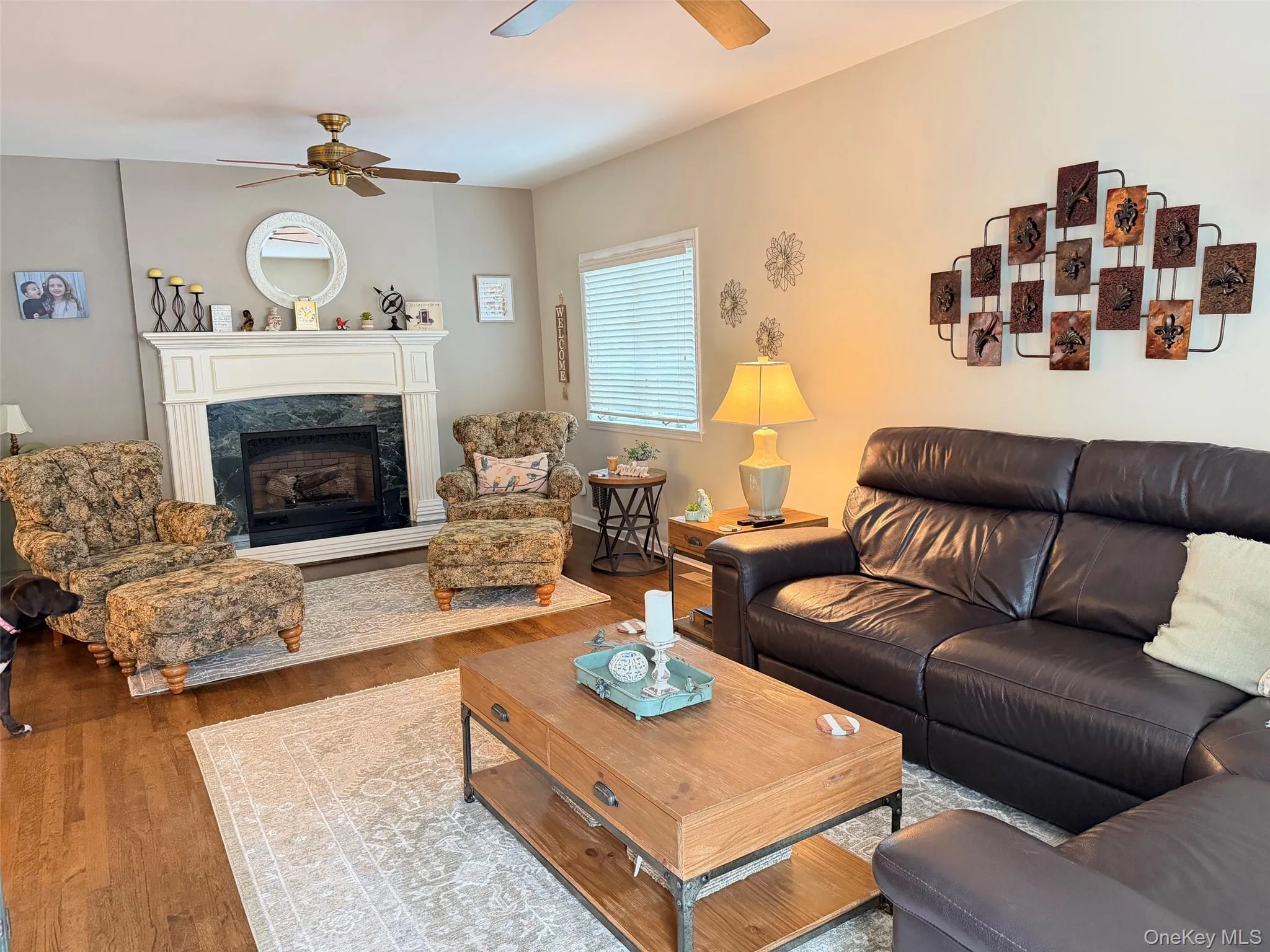 Living area featuring wood-finish flooring, a white mantel fireplace with a dark stone surround, and a ceiling fan Living area featuring wood-finish flooring, a white mantel fireplace with a dark stone surround, and a ceiling fan