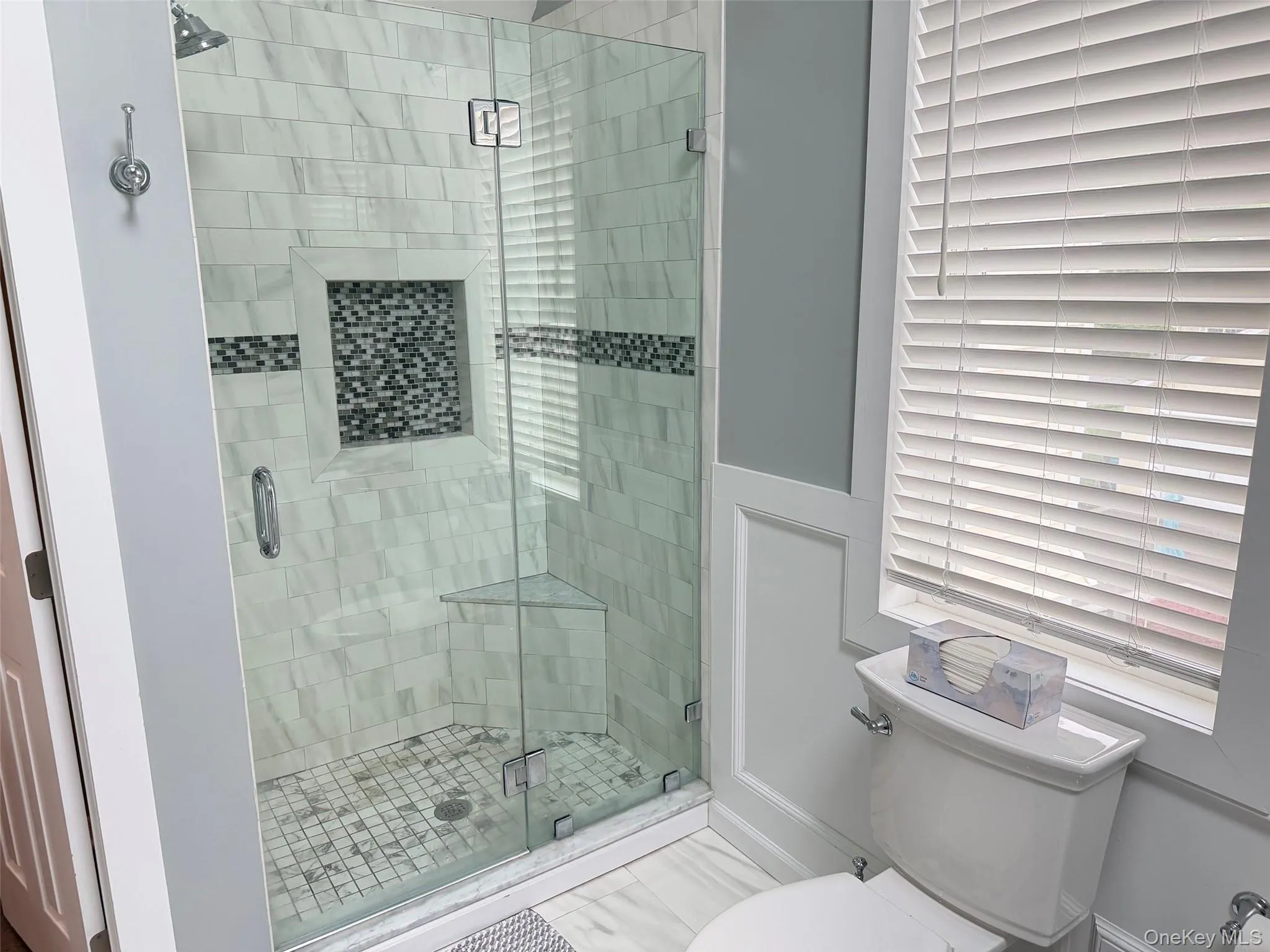 Frameless glass shower enclosure featuring white subway tile, mosaic accent band, and a built-in corner bench Frameless glass shower enclosure featuring white subway tile, mosaic accent band, and a built-in corner bench