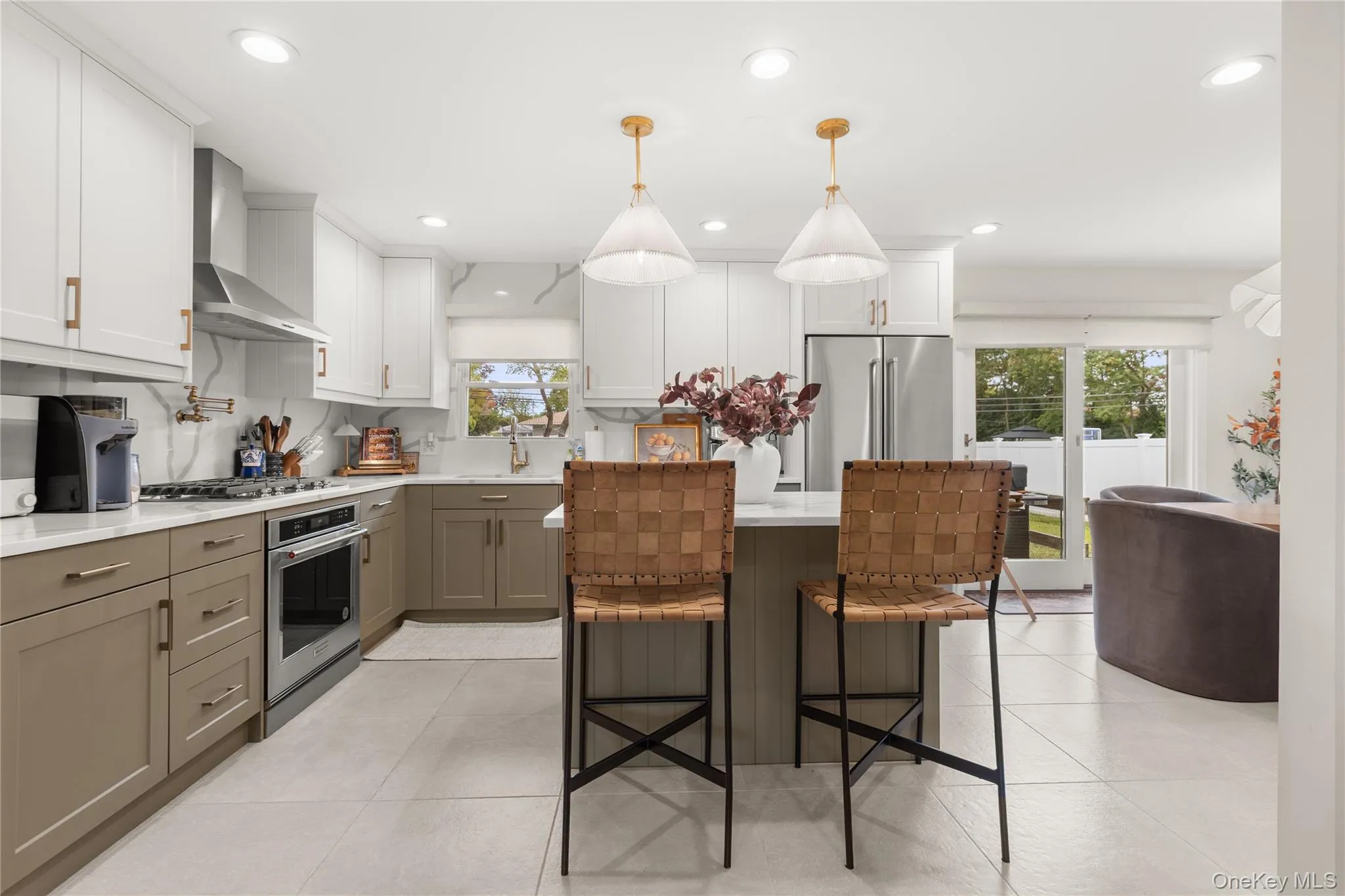 Kitchen with white cabinetry, pendant lighting, wall chimney range hood, light tile patterned floors, and appliances with stainless steel finishes Kitchen with white cabinetry, pendant lighting, wall chimney range hood, light tile patterned floors, and appliances with stainless steel finishes