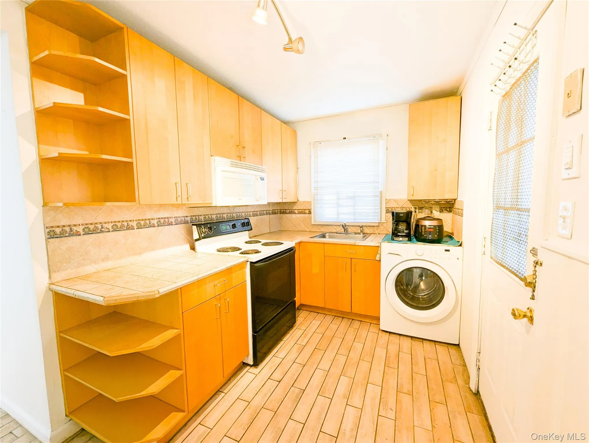 Kitchen featuring tile counters, light hardwood / wood-style floors, white appliances, washer / dryer, and decorative backsplash Kitchen featuring tile counters, light hardwood / wood-style floors, white appliances, washer / dryer, and decorative backsplash
