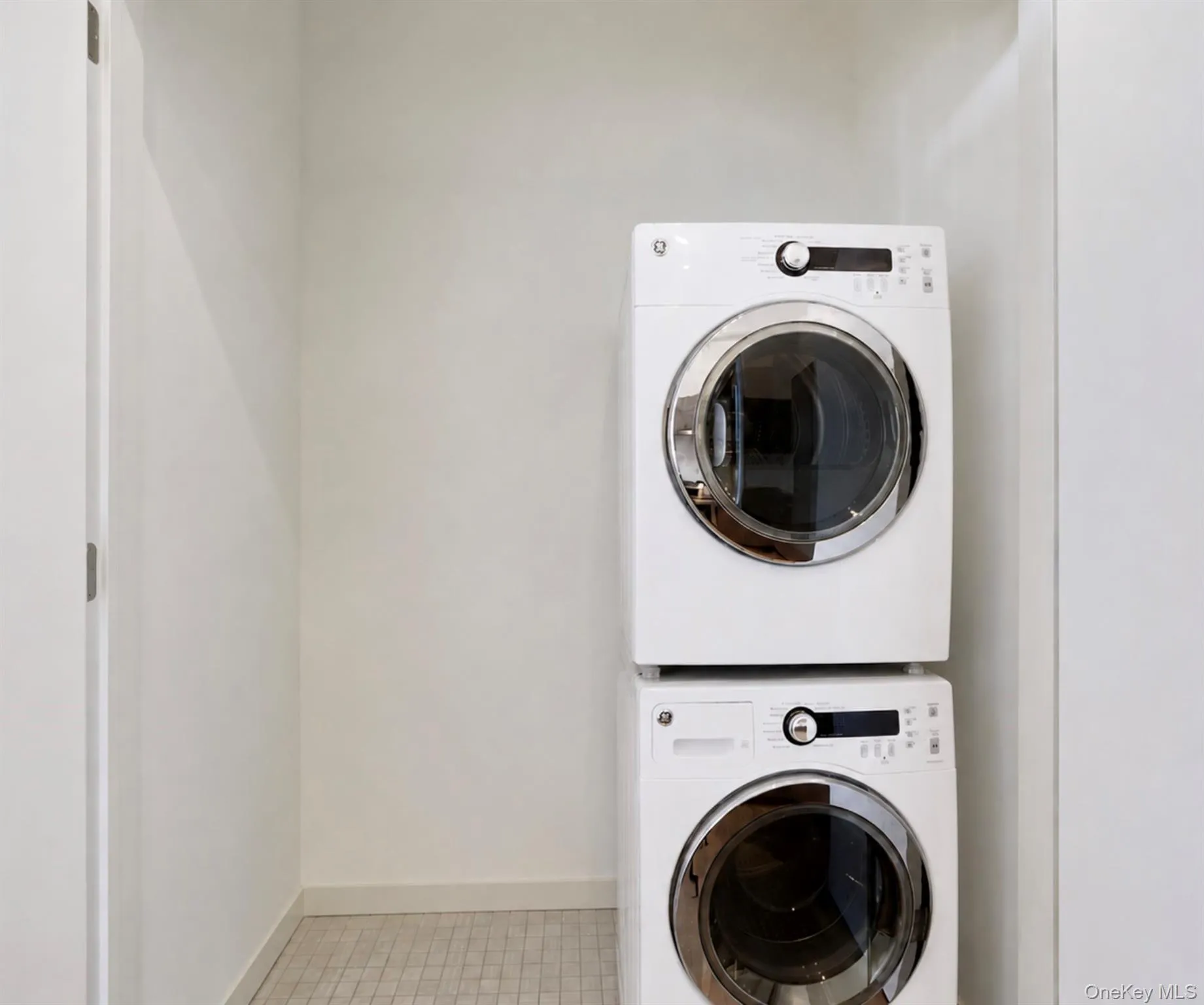In-unit laundry closet with tile floors, stacked washer and dryer, and storage space In-unit laundry closet with tile floors, stacked washer and dryer, and storage space