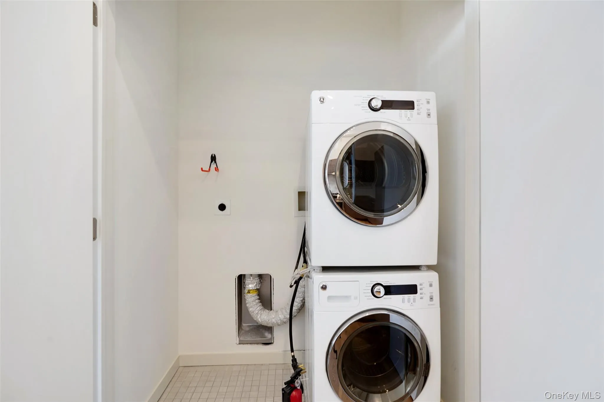 Laundry room with tile patterned floors, baseboards, stacked washer and clothes dryer, and laundry area Laundry room with tile patterned floors, baseboards, stacked washer and clothes dryer, and laundry area