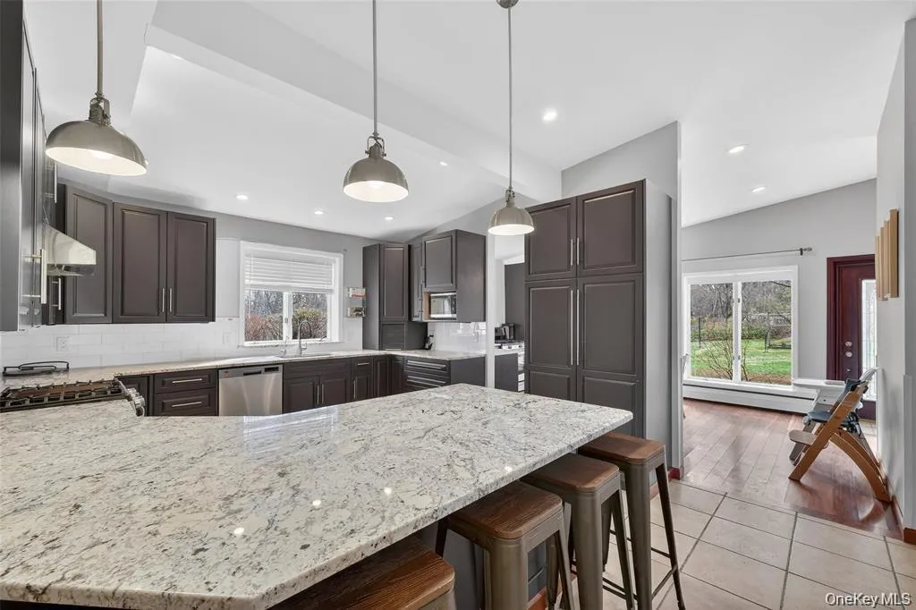 Kitchen with tasteful backsplash, a peninsula, a kitchen breakfast bar, light stone counters, and vaulted ceiling with beams Kitchen with tasteful backsplash, a peninsula, a kitchen breakfast bar, light stone counters, and vaulted ceiling with beams