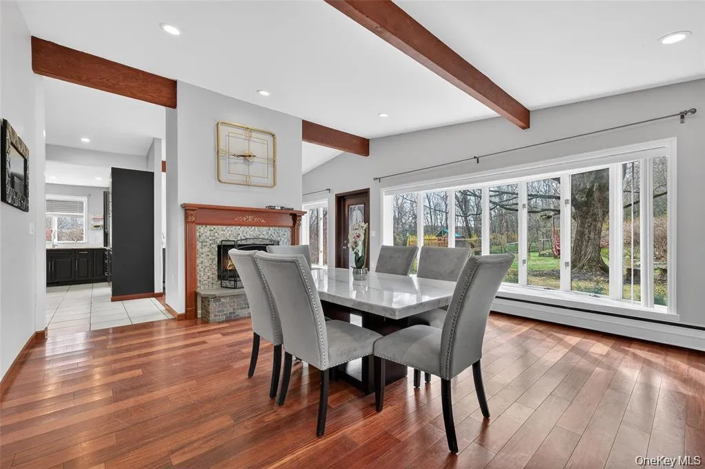 Dining space featuring a lit fireplace, recessed lighting, vaulted ceiling with beams, light wood finished floors, and a baseboard heating unit Dining space featuring a lit fireplace, recessed lighting, vaulted ceiling with beams, light wood finished floors, and a baseboard heating unit
