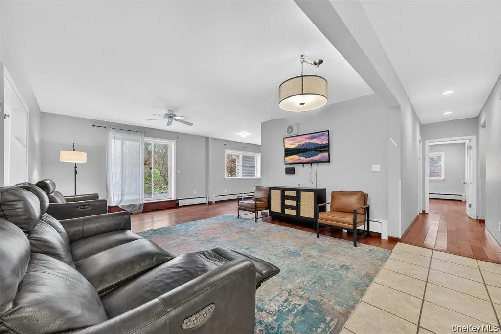 Living room featuring healthy amount of natural light, ceiling fan, tile patterned flooring, and a baseboard heating unit Living room featuring healthy amount of natural light, ceiling fan, tile patterned flooring, and a baseboard heating unit