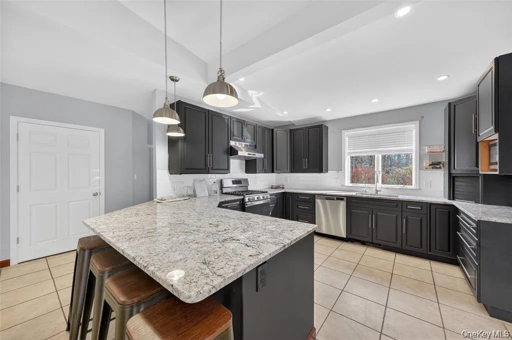 Kitchen featuring a kitchen breakfast bar, backsplash, a peninsula, stainless steel appliances, and light stone counters Kitchen featuring a kitchen breakfast bar, backsplash, a peninsula, stainless steel appliances, and light stone counters