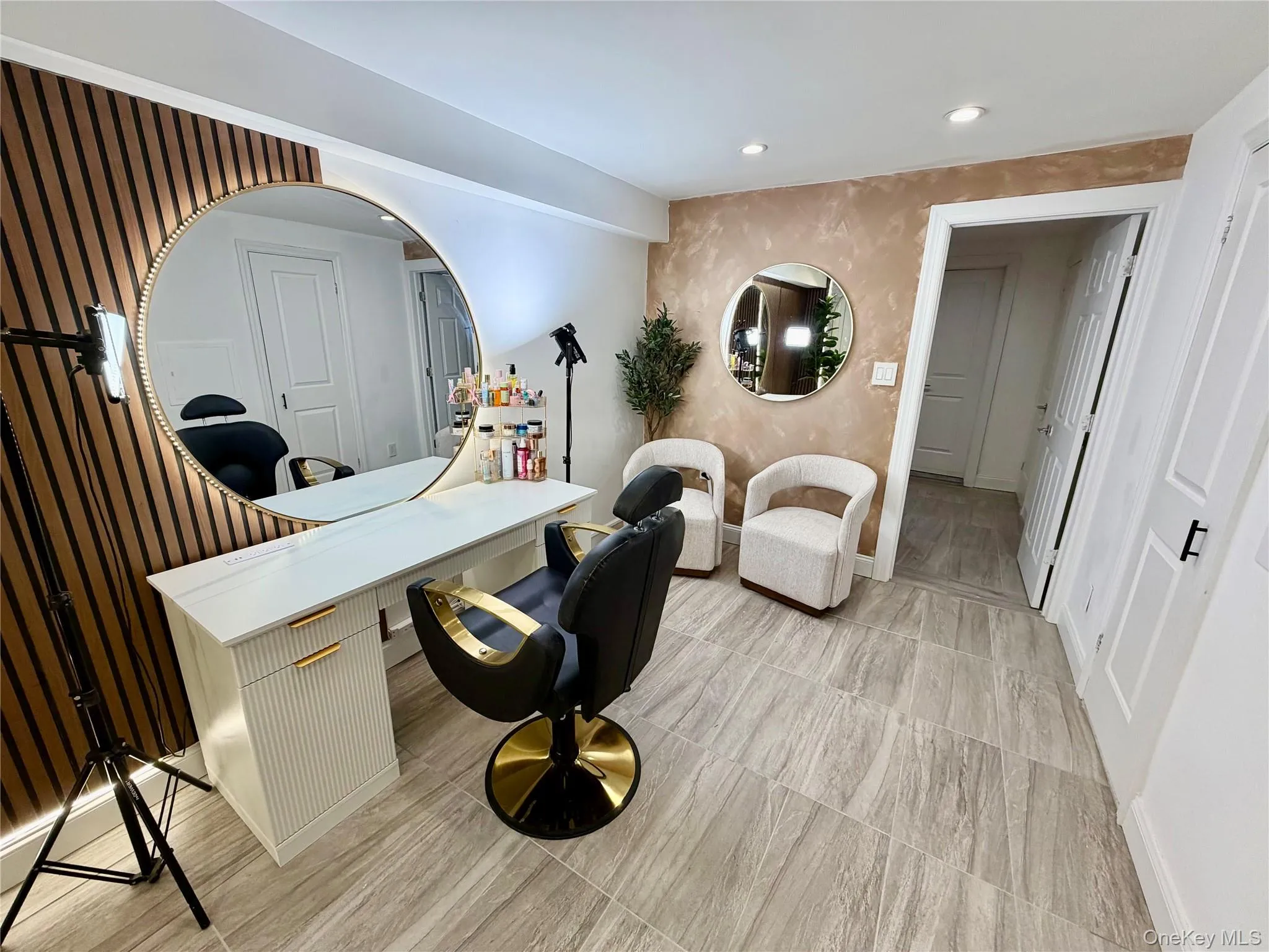 Spacious room featuring wood-finish accent wall, large circular mirror, recessed lighting, and light-toned tile flooring Spacious room featuring wood-finish accent wall, large circular mirror, recessed lighting, and light-toned tile flooring