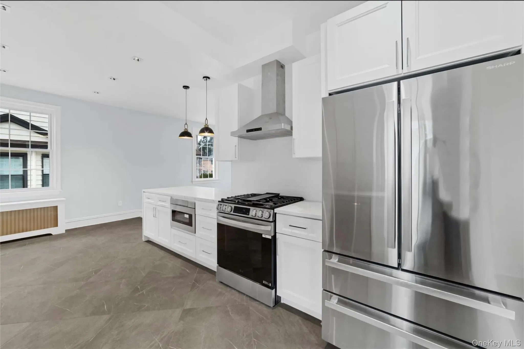 Contemporary kitchen featuring white cabinetry, stainless steel appliances, a center island with pendant lighting, and large format floor tiling Contemporary kitchen featuring white cabinetry, stainless steel appliances, a center island with pendant lighting, and large format floor tiling