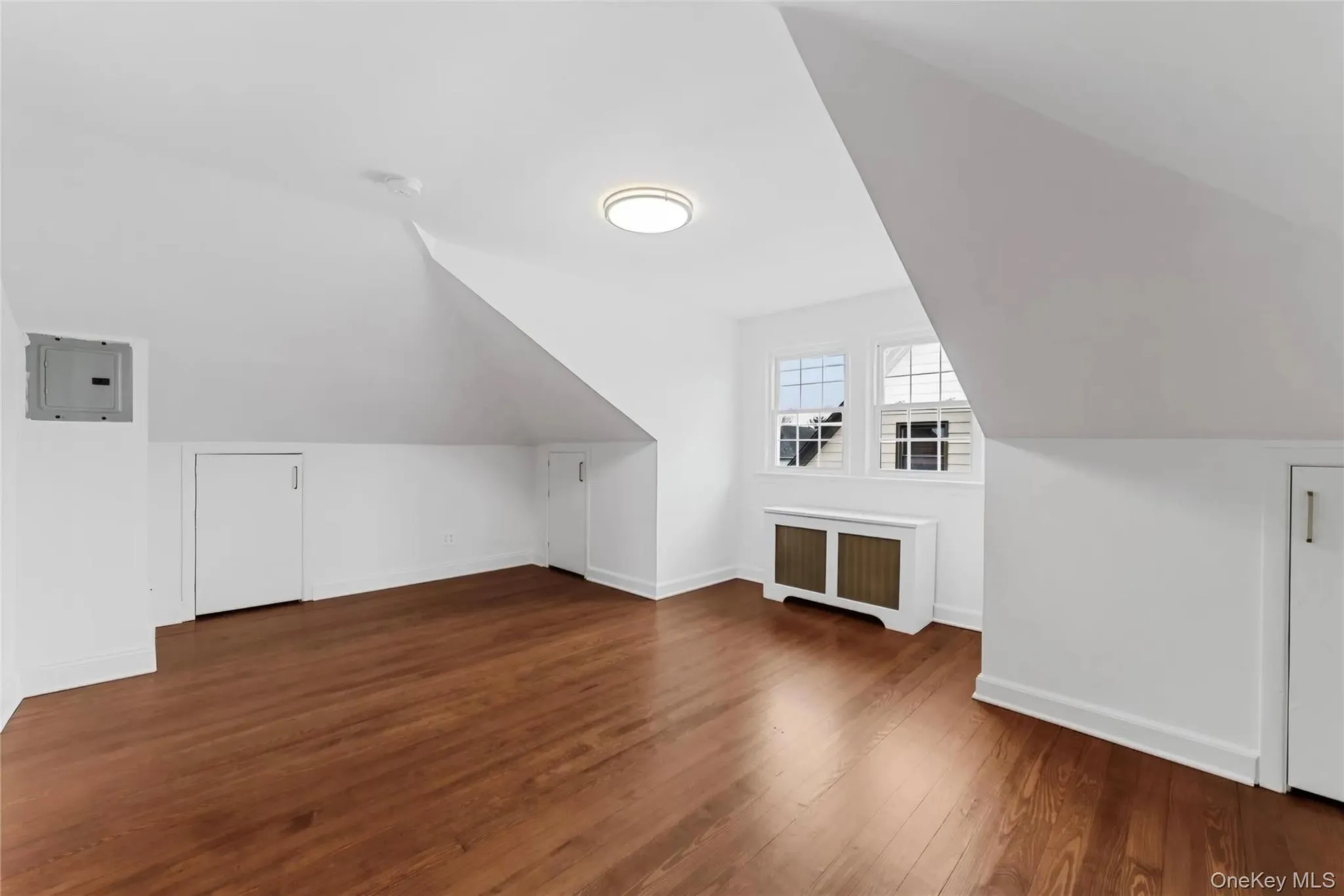 Room featuring wood-finish flooring, white baseboards, and two multi-pane windows Room featuring wood-finish flooring, white baseboards, and two multi-pane windows