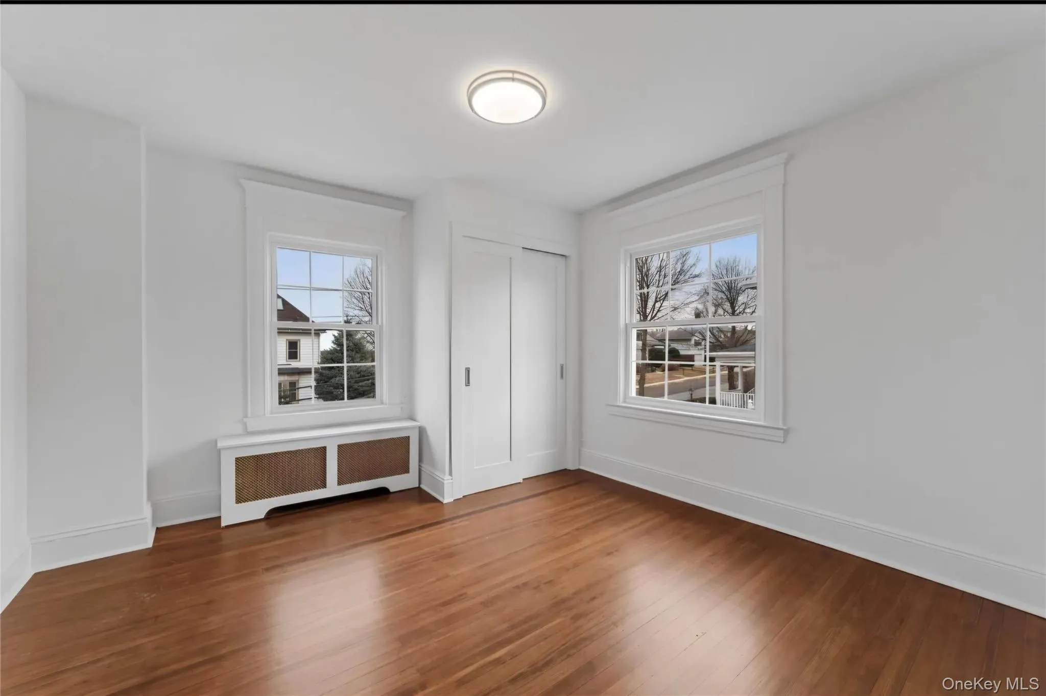 Room featuring wood-finish flooring, white baseboards, and two multi-pane windows Room featuring wood-finish flooring, white baseboards, and two multi-pane windows