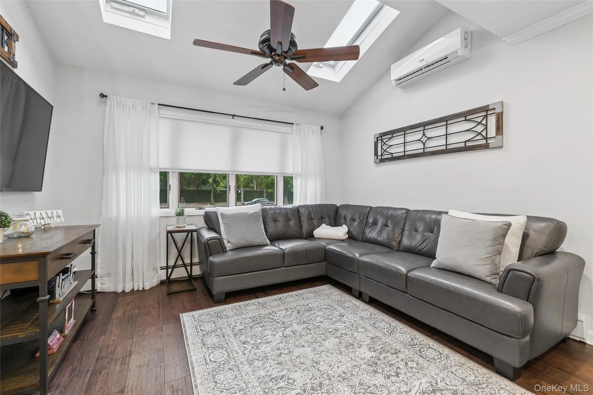 Living area featuring vaulted ceilings with skylights, wood-finish flooring, and a ceiling fan Living area featuring vaulted ceilings with skylights, wood-finish flooring, and a ceiling fan