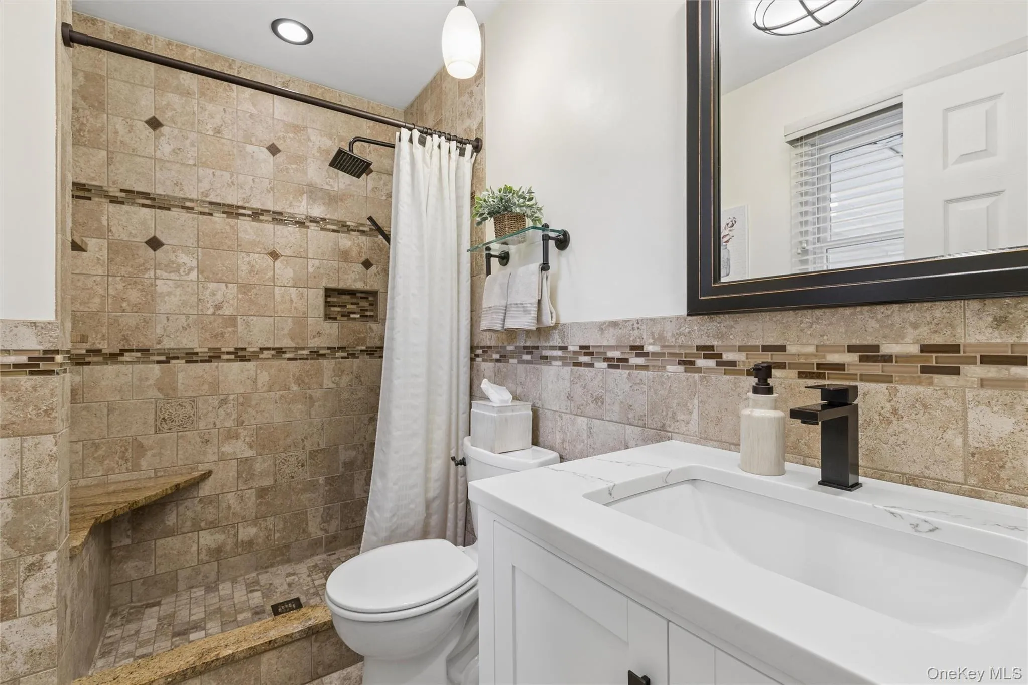 Shower featuring natural stone-look tile, mosaic accent bands, a built-in bench, and a niche Shower featuring natural stone-look tile, mosaic accent bands, a built-in bench, and a niche