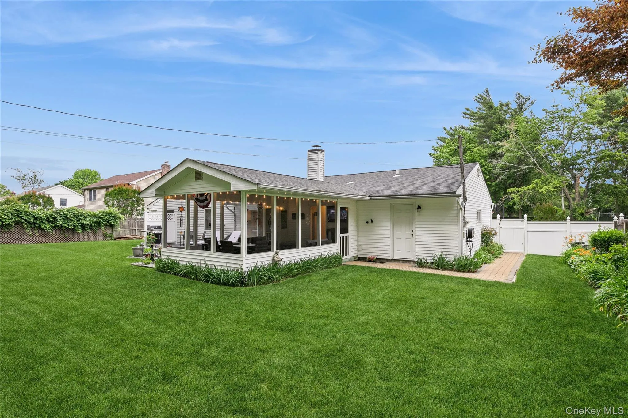 Expansive green lawn featuring a screened porch, white siding, a paved walkway, and a white privacy fence Expansive green lawn featuring a screened porch, white siding, a paved walkway, and a white privacy fence