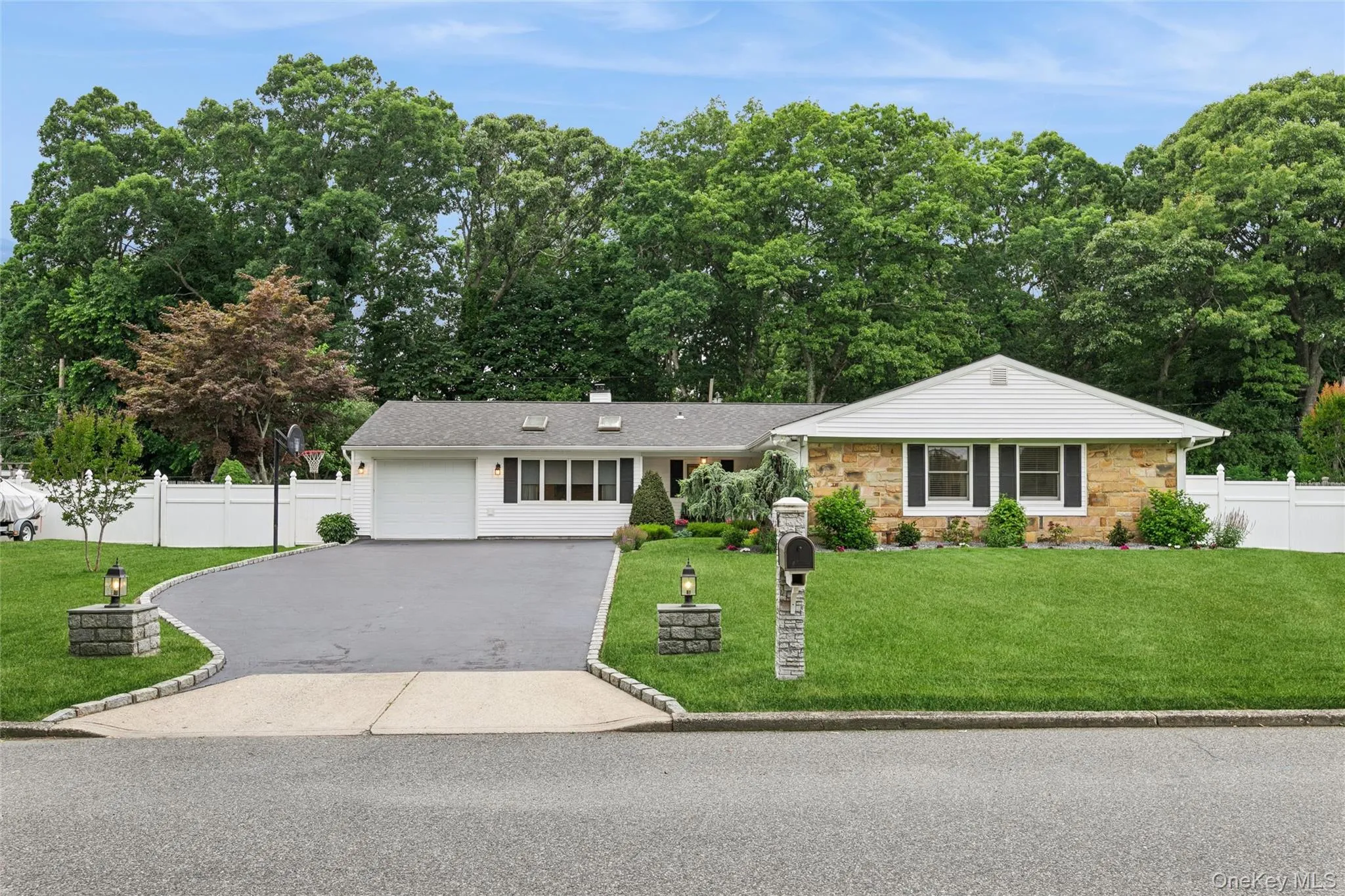 Ranch-style residence featuring a stone and white siding exterior, a manicured lawn, and a paved driveway Ranch-style residence featuring a stone and white siding exterior, a manicured lawn, and a paved driveway