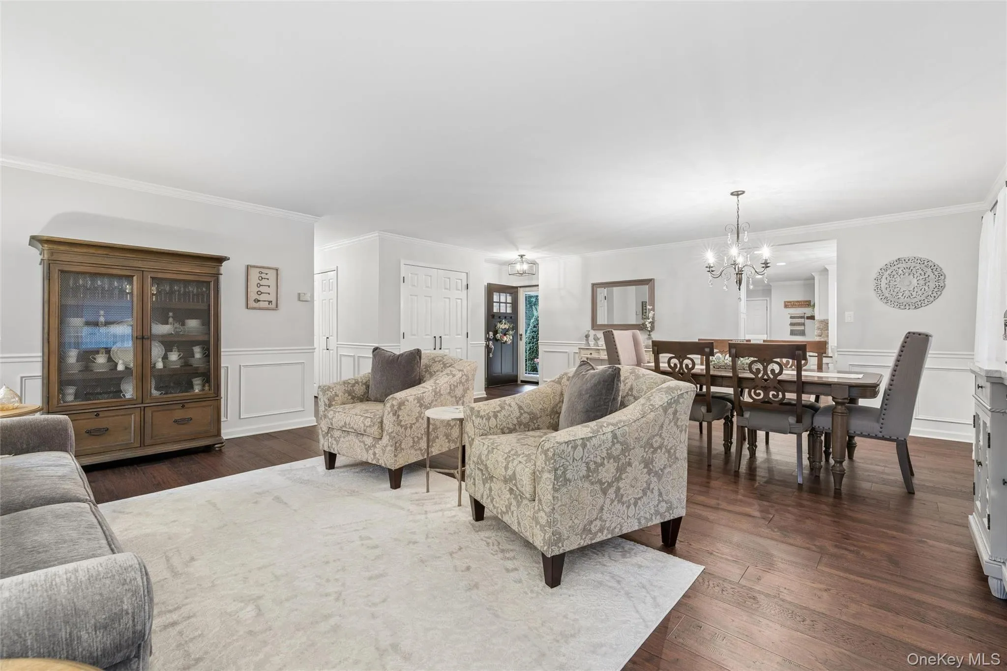 Spacious living area featuring wood-finish flooring, white wall paneling, and crown molding Spacious living area featuring wood-finish flooring, white wall paneling, and crown molding
