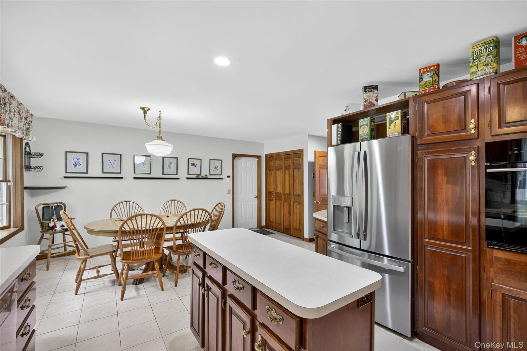 Kitchen with stainless steel fridge with ice dispenser, oven, light countertops, a kitchen island, and light tile patterned floors Kitchen with stainless steel fridge with ice dispenser, oven, light countertops, a kitchen island, and light tile patterned floors