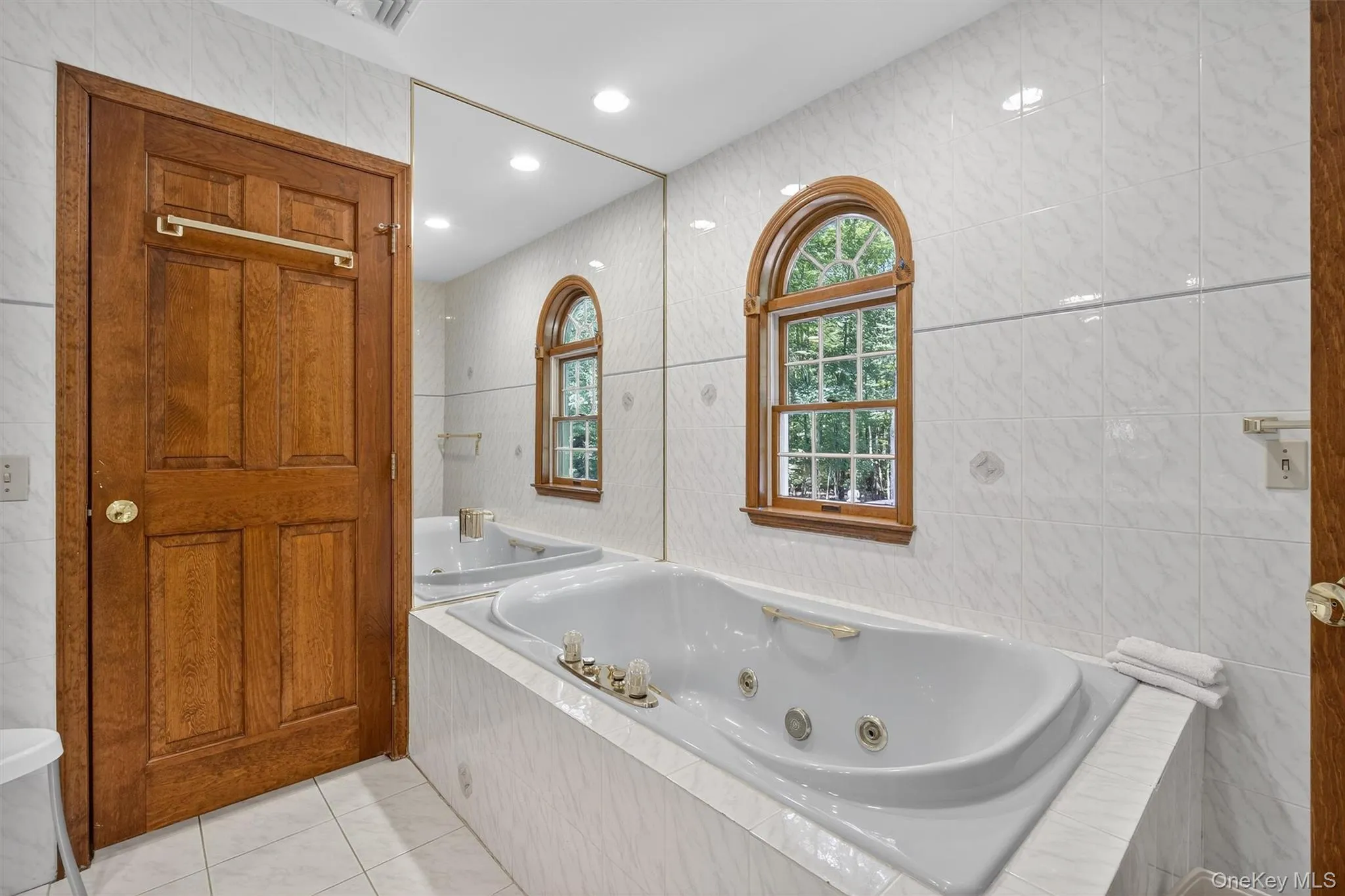 Full bath featuring tile walls, a tub with jets, and tile patterned floors Full bath featuring tile walls, a tub with jets, and tile patterned floors