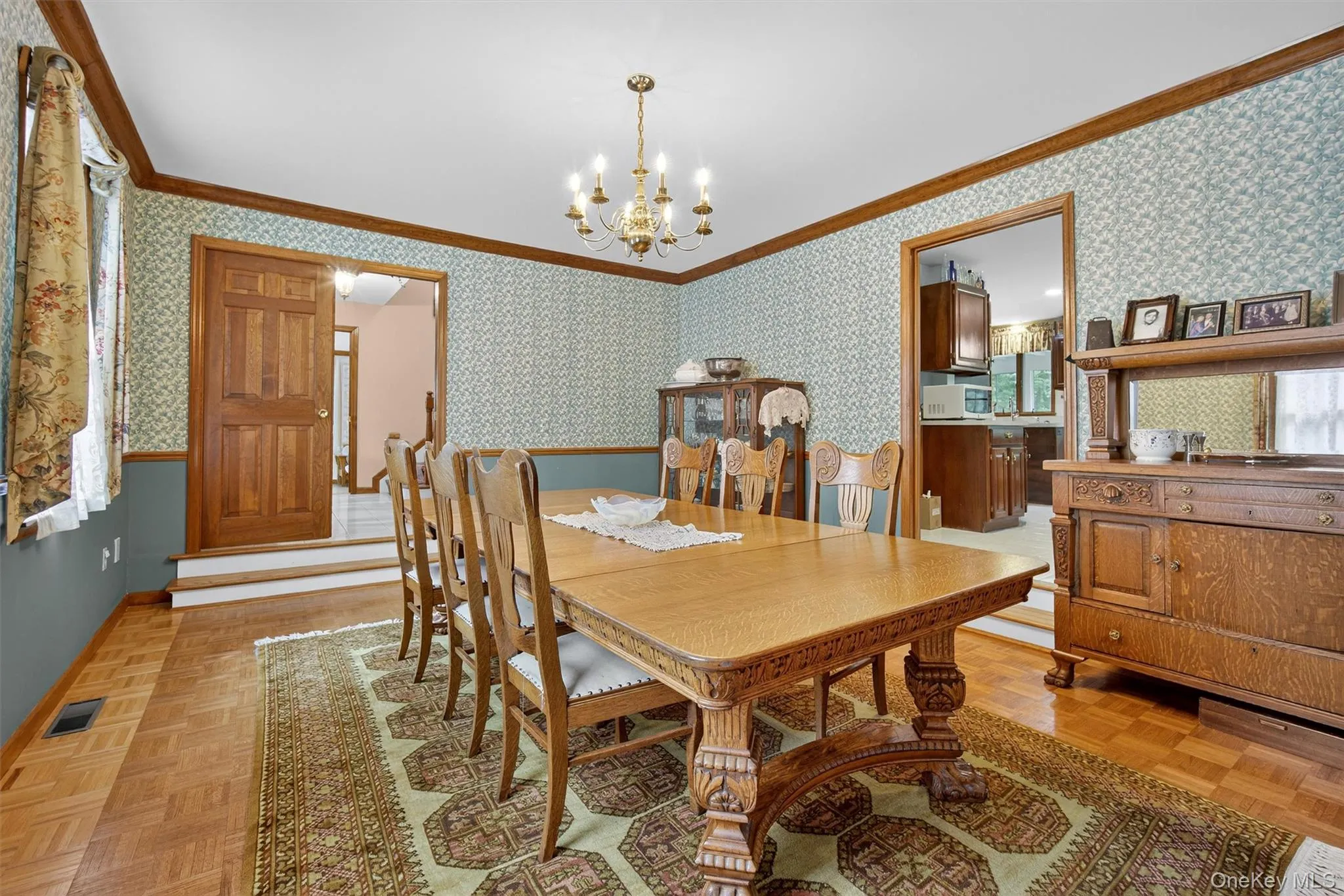 Dining space featuring crown molding, wallpapered walls, and a chandelier Dining space featuring crown molding, wallpapered walls, and a chandelier
