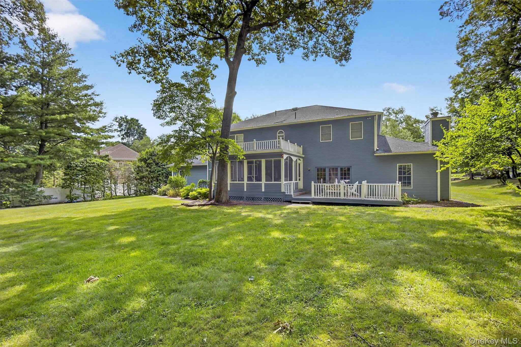 Back of house featuring a chimney, a sunroom, a yard, a deck, and a shingled roof Back of house featuring a chimney, a sunroom, a yard, a deck, and a shingled roof