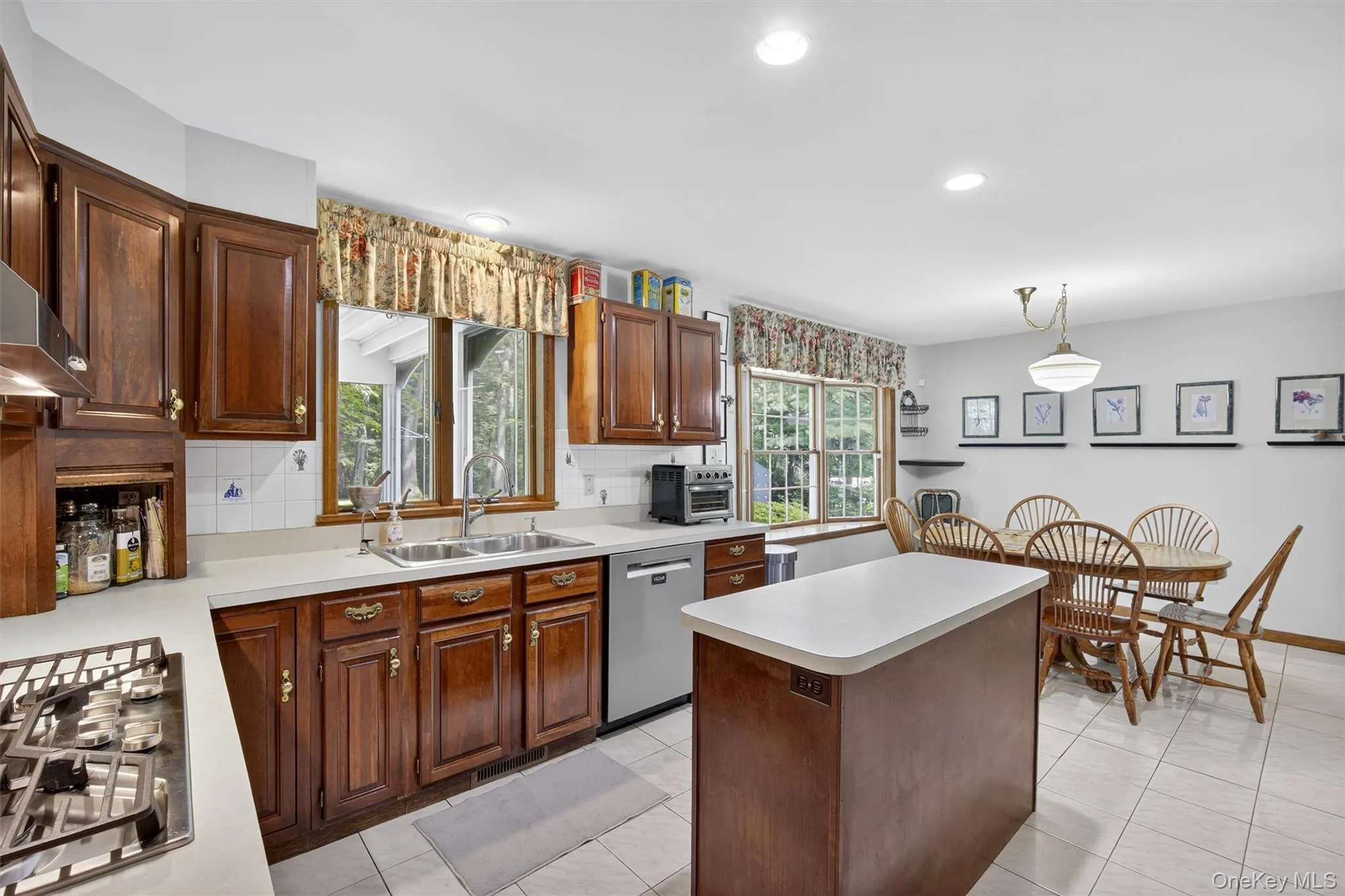 Kitchen with appliances with stainless steel finishes, light countertops, a kitchen island, decorative backsplash, and light tile patterned floors Kitchen with appliances with stainless steel finishes, light countertops, a kitchen island, decorative backsplash, and light tile patterned floors