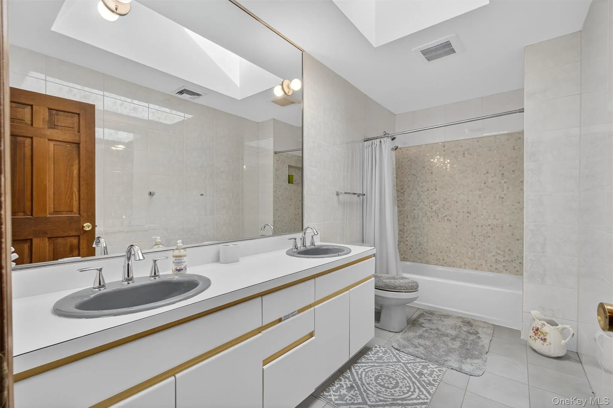Full bathroom featuring shower / bathtub combination with curtain, tile patterned flooring, double vanity, and a skylight Full bathroom featuring shower / bathtub combination with curtain, tile patterned flooring, double vanity, and a skylight