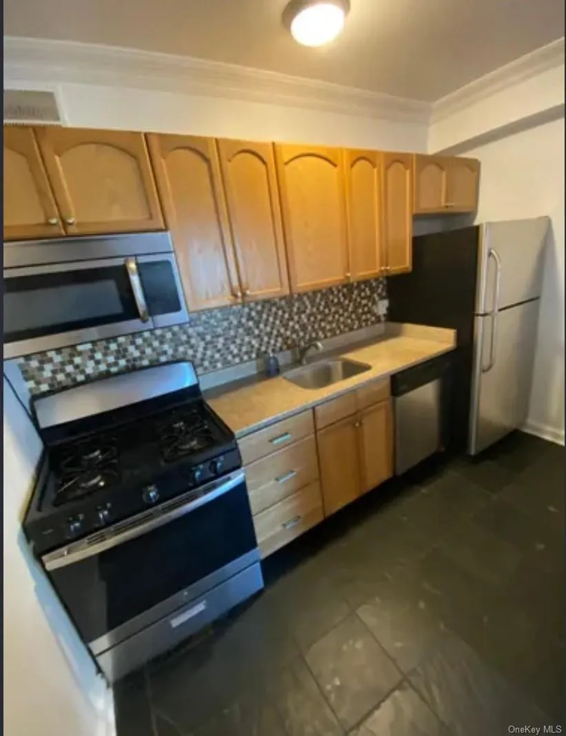 Kitchen with stainless steel appliances, a sink, ornamental molding, tasteful backsplash, and light countertops Kitchen with stainless steel appliances, a sink, ornamental molding, tasteful backsplash, and light countertops