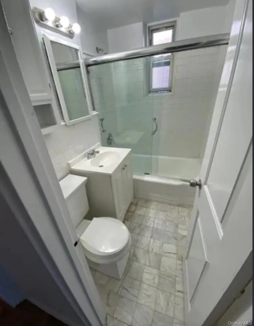 Bathroom with toilet, marble finish flooring, enclosed tub / shower combo, and vanity Bathroom with toilet, marble finish flooring, enclosed tub / shower combo, and vanity