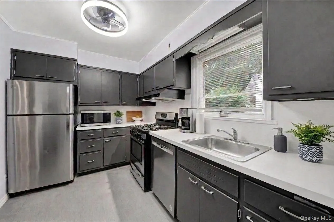 Kitchen featuring dark cabinetry, stainless steel appliances, white countertops, and a ceiling light fixture with a fan Kitchen featuring dark cabinetry, stainless steel appliances, white countertops, and a ceiling light fixture with a fan