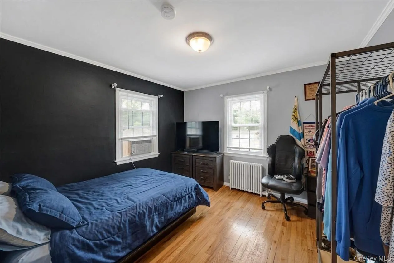 2nd first floor bedroom with hardwood flooring throughout featuring two windows with white trim, a built-in radiator, and a ceiling-mounted light fixture 2nd first floor bedroom with hardwood flooring throughout featuring two windows with white trim, a built-in radiator, and a ceiling-mounted light fixture