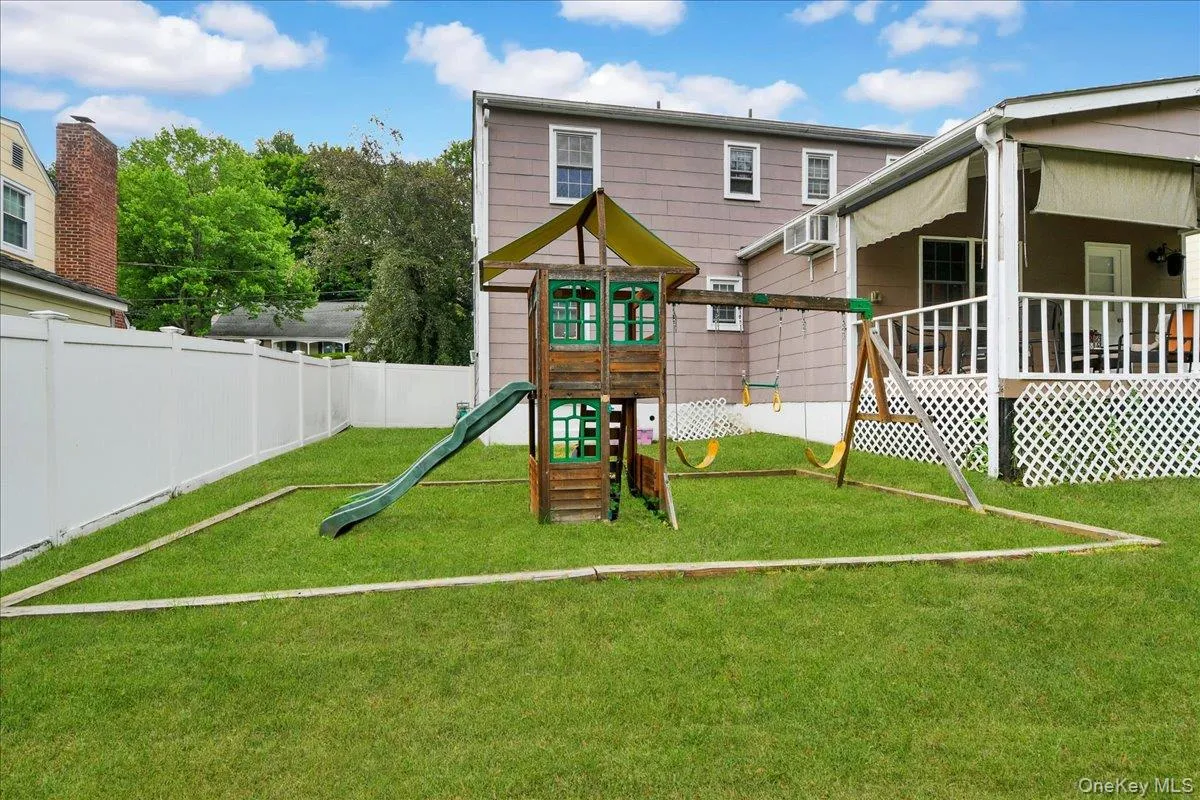 Expansive green lawn featuring a wooden playset with slide and swings, a white privacy fence, and a covered porch with white lattice skirting Expansive green lawn featuring a wooden playset with slide and swings, a white privacy fence, and a covered porch with white lattice skirting