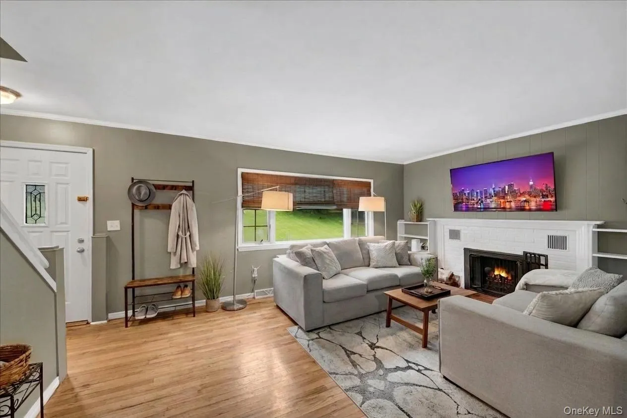 Living area featuring wood-finish flooring, a white trim fireplace with a black insert, and built-in shelving Living area featuring wood-finish flooring, a white trim fireplace with a black insert, and built-in shelving