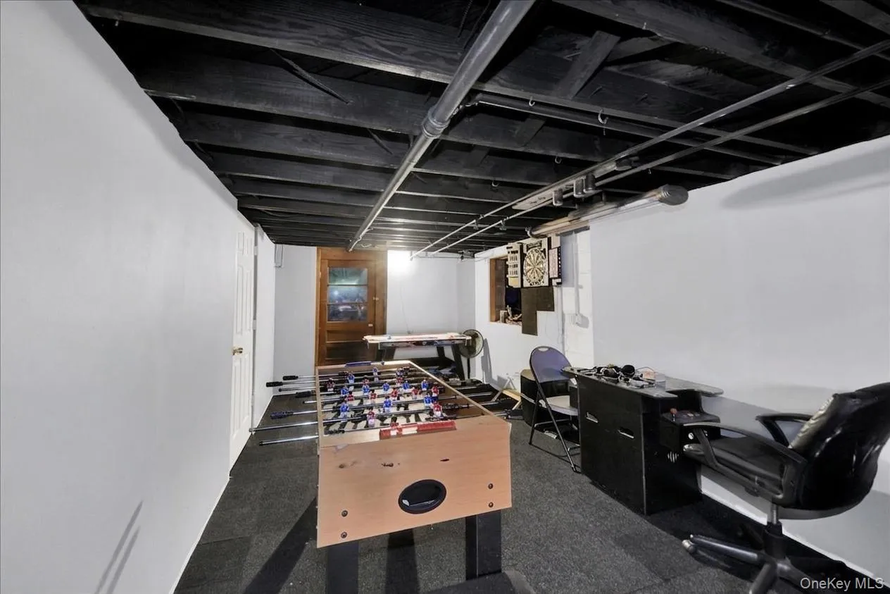 Finished basement space with exposed black ceiling joists, white painted walls, and dark gray flooring Finished basement space with exposed black ceiling joists, white painted walls, and dark gray flooring