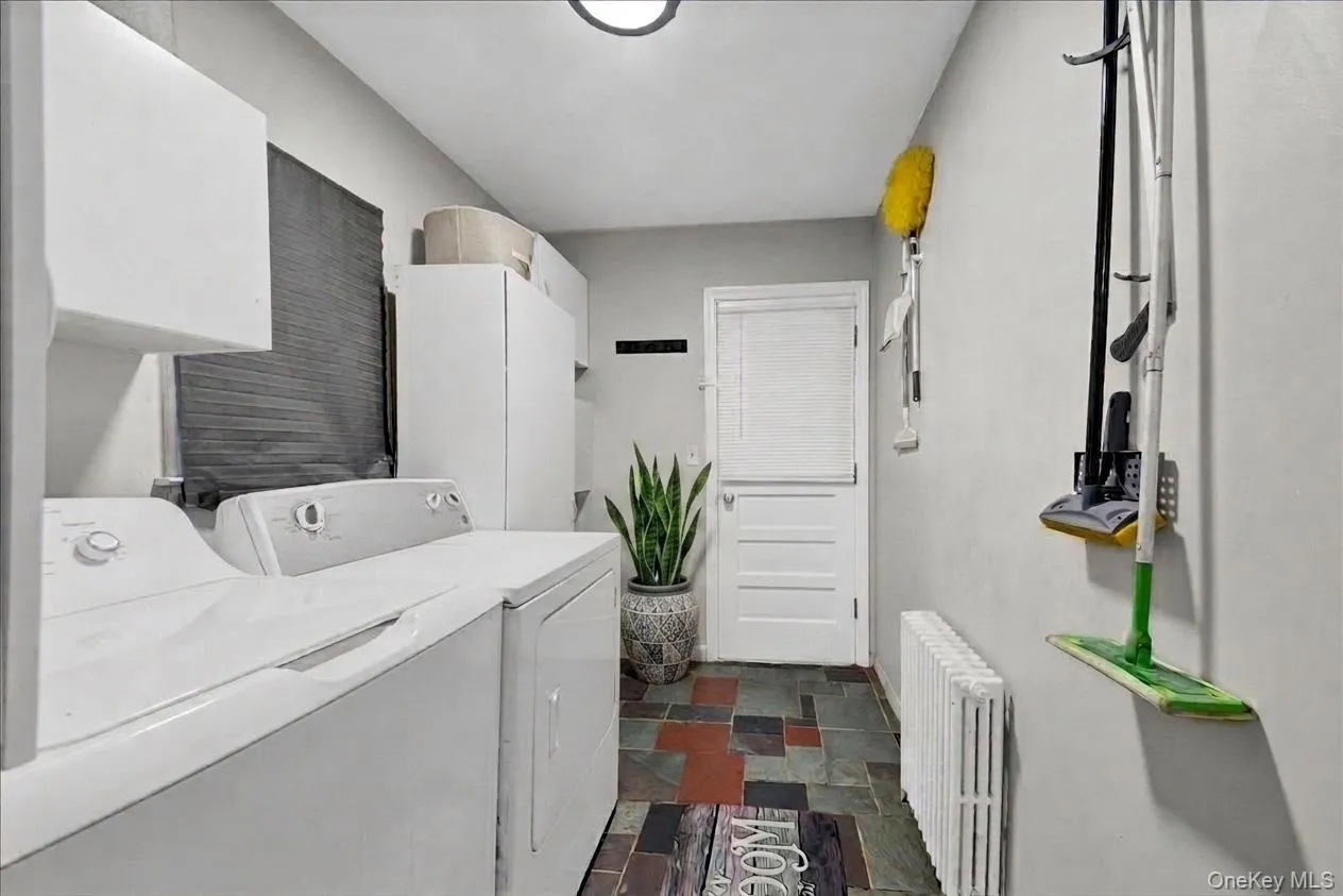 Laundry area with access through the kitchen and walk-out access onto the back covered deck; featuring multi-toned slate-style flooring, white upper cabinetry, and a window with blinds Laundry area with access through the kitchen and walk-out access onto the back covered deck; featuring multi-toned slate-style flooring, white upper cabinetry, and a window with blinds