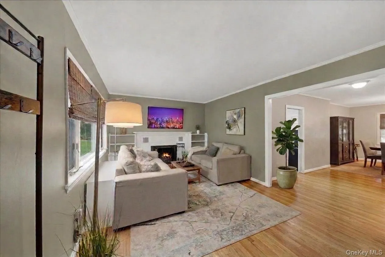 Living area featuring wood-finish flooring, a fireplace with a mantel, built-in shelving, and crown molding Living area featuring wood-finish flooring, a fireplace with a mantel, built-in shelving, and crown molding