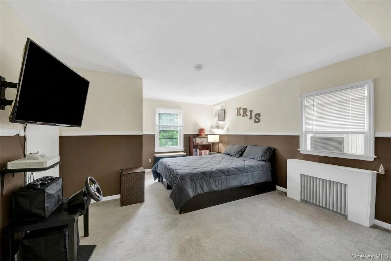 Carpeted primary bedroom featuring a built-in window air conditioning unit, white trim, and a window with blinds Carpeted primary bedroom featuring a built-in window air conditioning unit, white trim, and a window with blinds