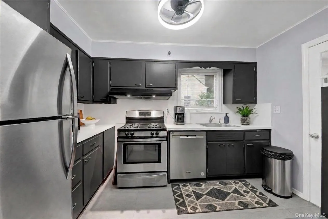 Modern kitchen featuring stainless steel appliances, dark cabinetry, light countertops, and a ceiling fan with integrated lighting Modern kitchen featuring stainless steel appliances, dark cabinetry, light countertops, and a ceiling fan with integrated lighting