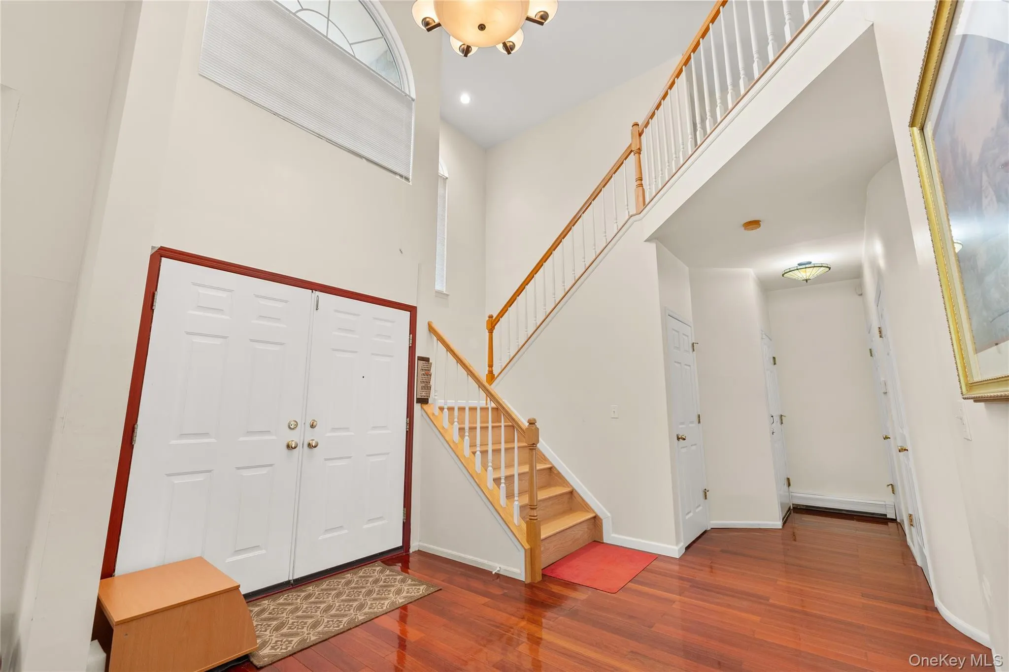 Two-story foyer featuring hardwood flooring, a white spindle staircase with wood handrails, and a grand arched transom window above double entry doors Two-story foyer featuring hardwood flooring, a white spindle staircase with wood handrails, and a grand arched transom window above double entry doors