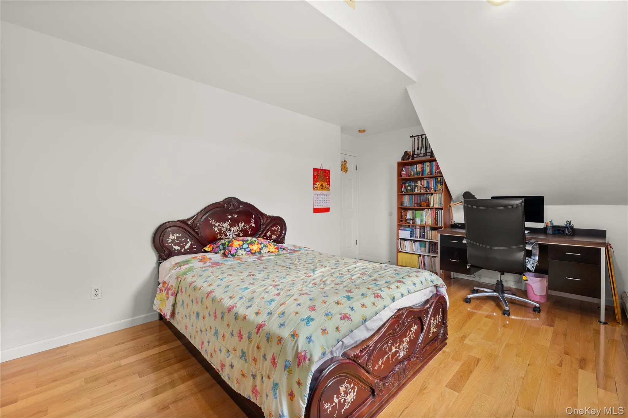 Bedroom featuring light wood-finish flooring, white walls, and an angled ceiling Bedroom featuring light wood-finish flooring, white walls, and an angled ceiling