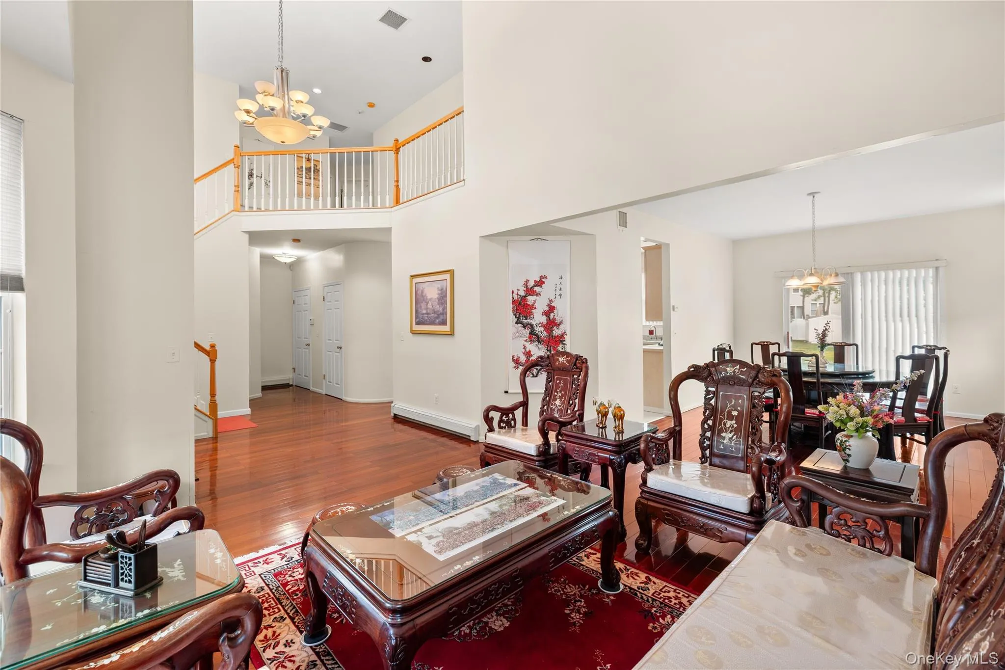 Two-story living area featuring wood-finish flooring, a grand chandelier, and a second-story overlook with white balusters Two-story living area featuring wood-finish flooring, a grand chandelier, and a second-story overlook with white balusters